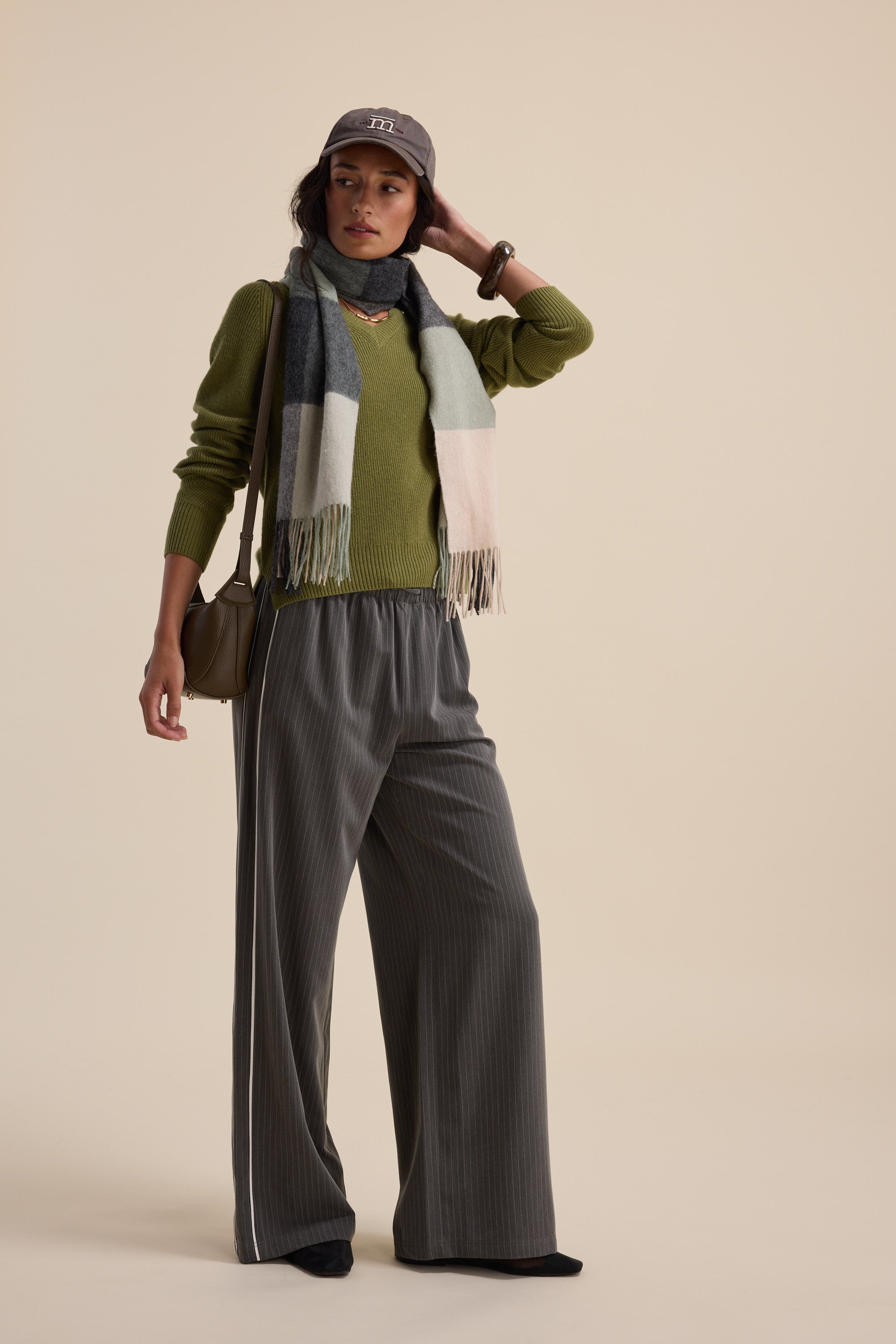 Person in an Elementary V Neck Cashmere Blend Sweater, gray wide-leg pants, scarf, and cap.