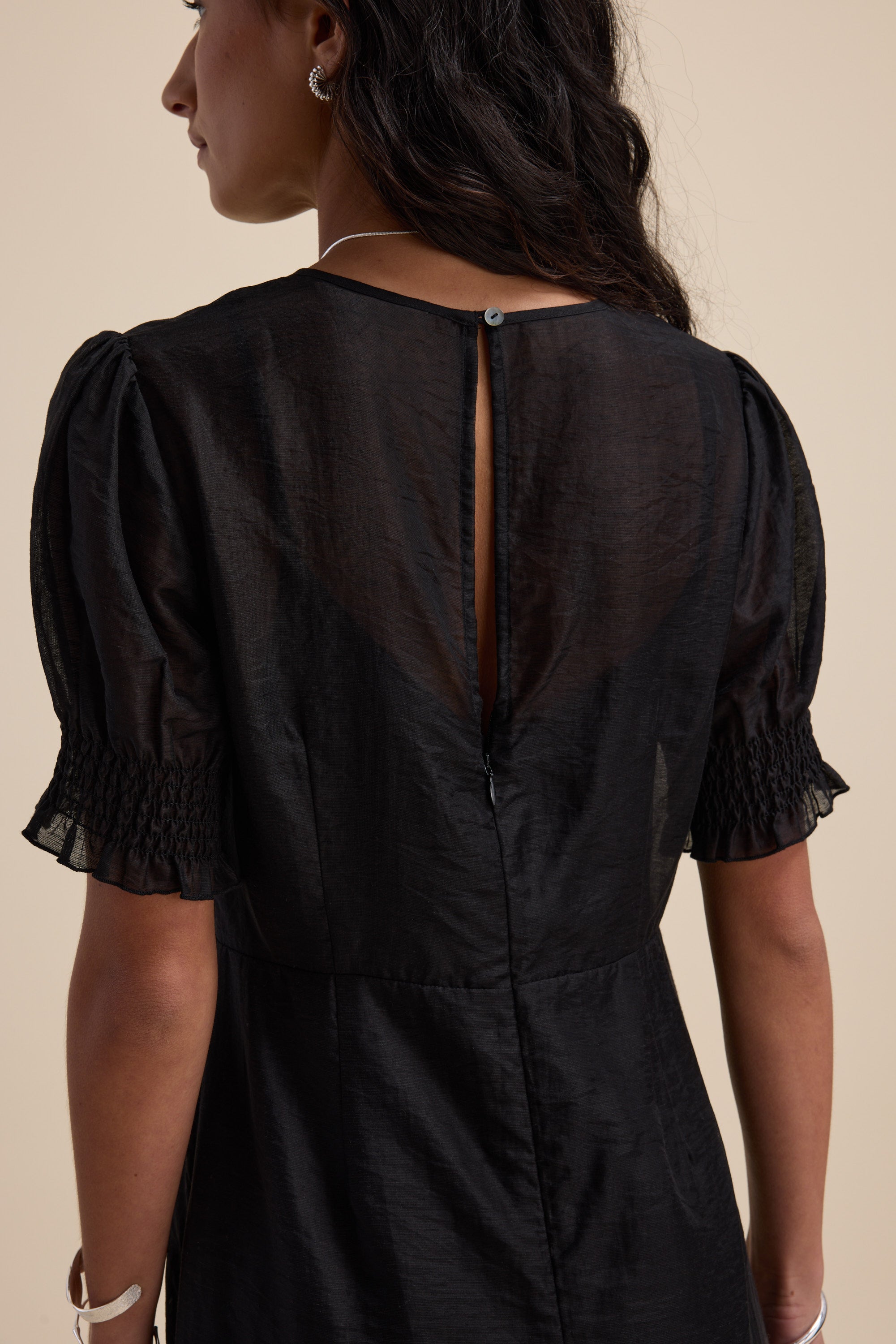 Woman wearing The Sheer Layering Dress by Max, shown from the back against a beige background.