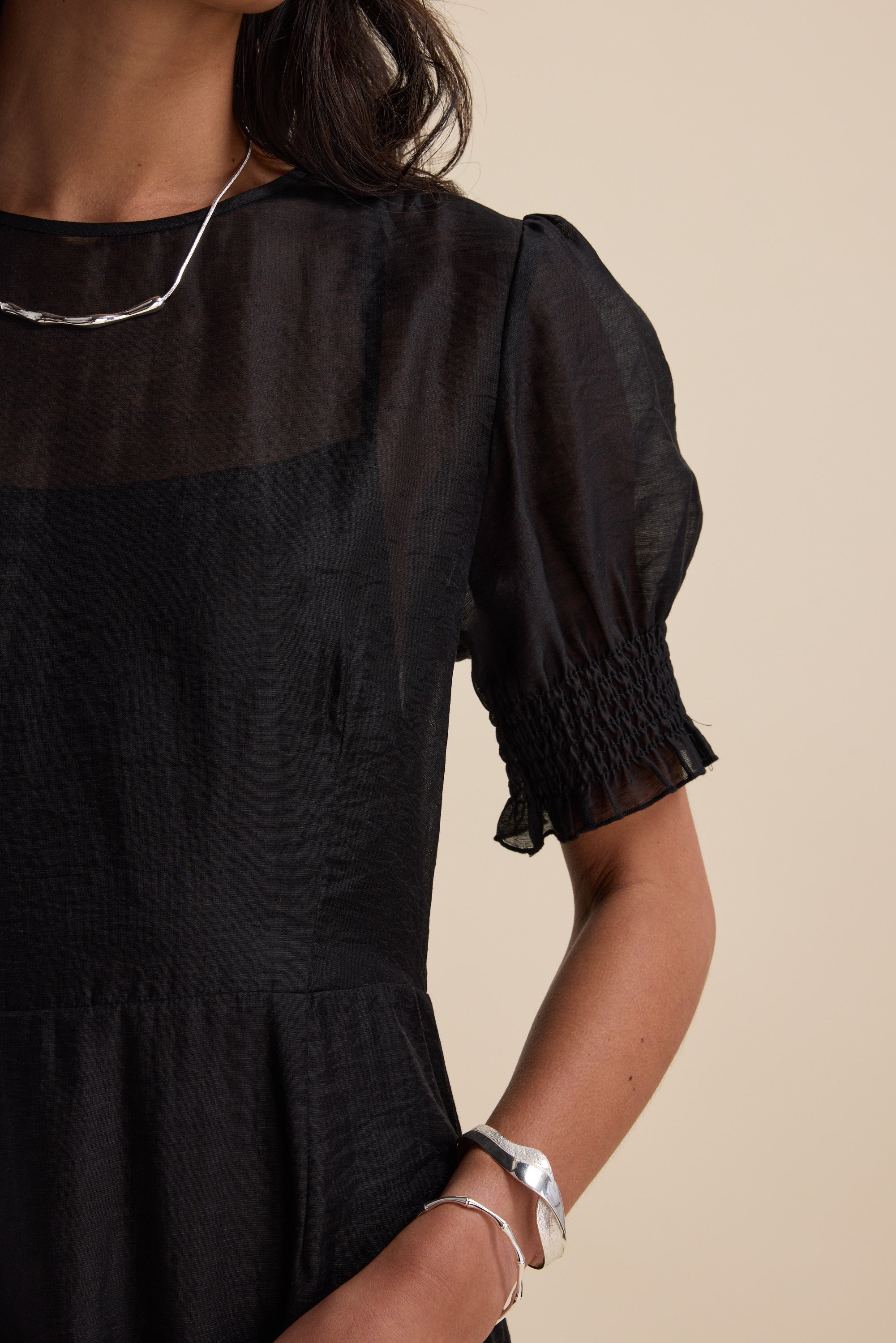 Woman in The Sheer Layering Dress by Max with silver jewelry on a beige background.