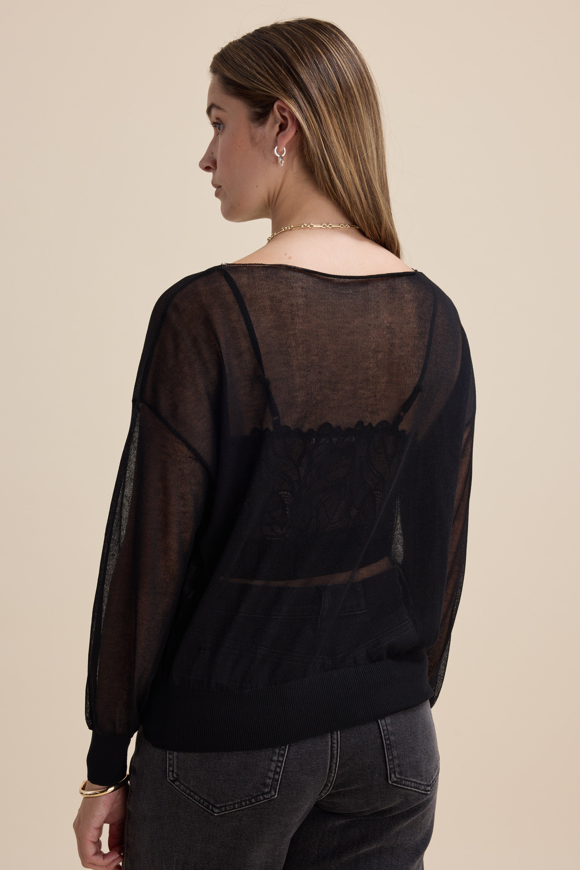 Model in Max Addie Sheer Knitted Top and dark jeans, back view against a beige background.