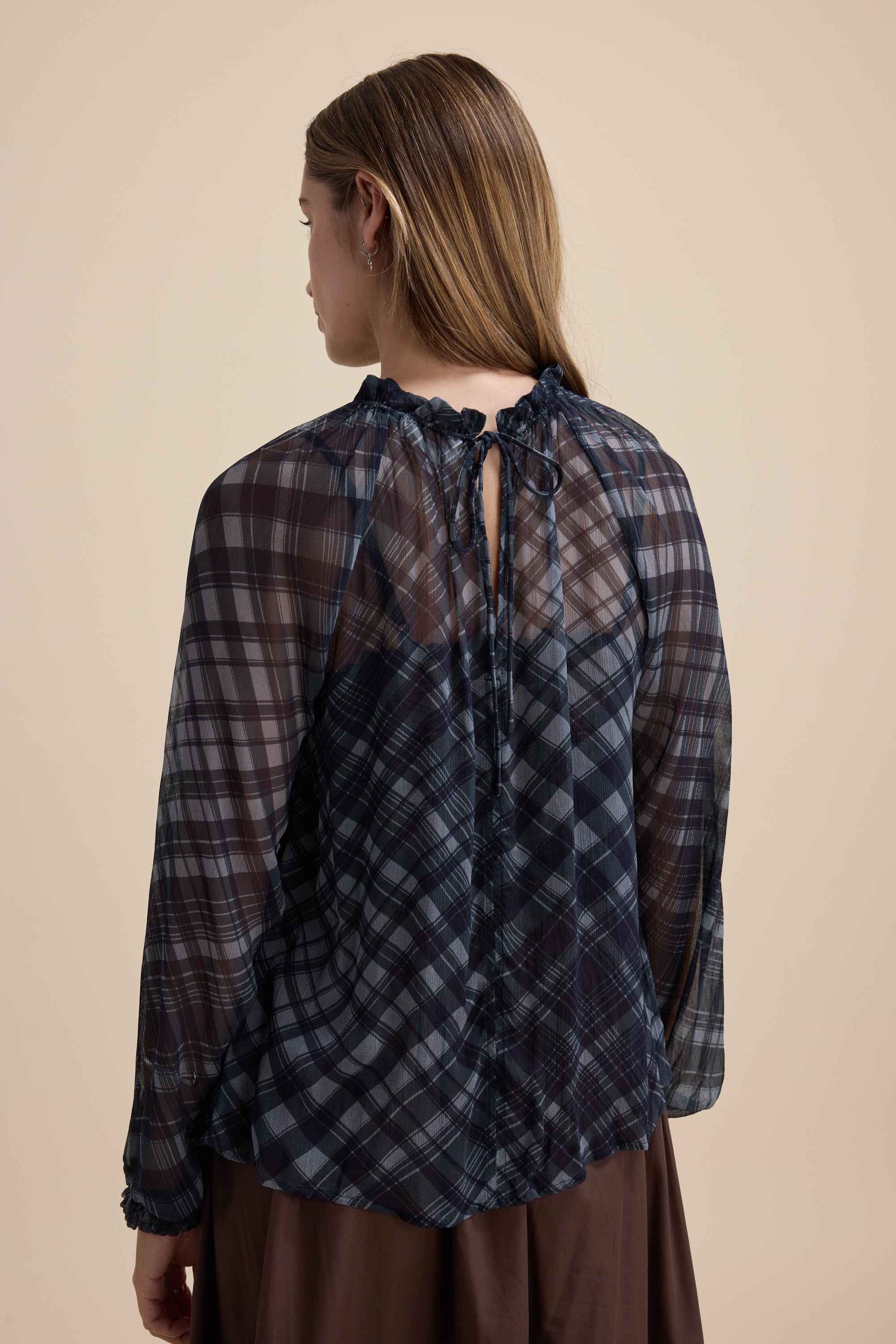 Woman in Max Quinn Gather Detail Blouse, navy check, puff sleeves, tie back, facing away.