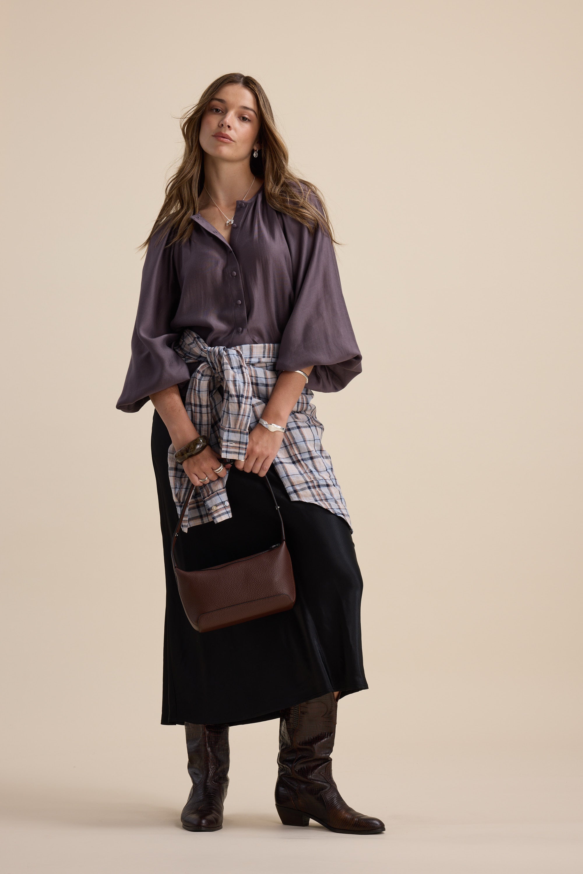 Woman in Max Vivian Button Front Blouse, long skirt, boots, plaid shirt at waist, brown purse.