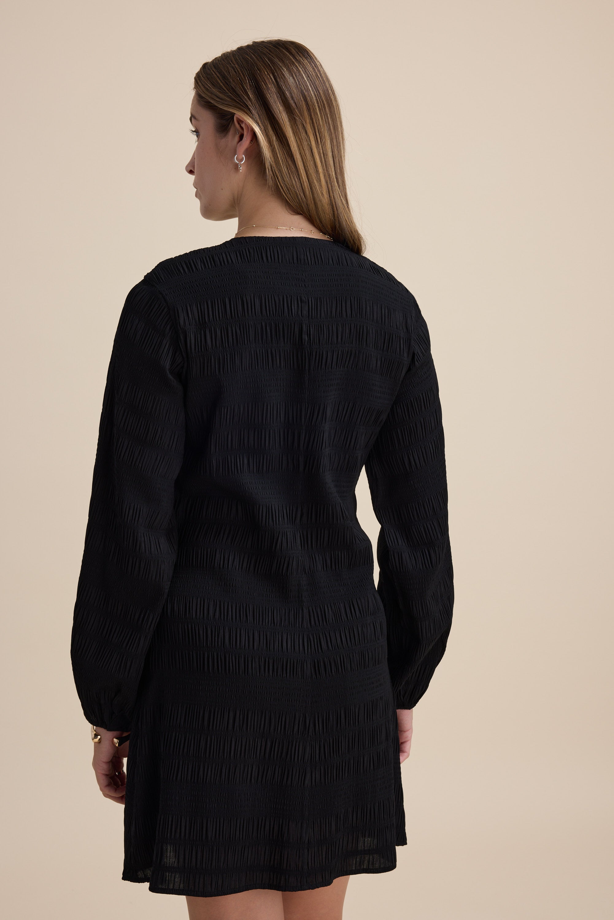 Woman with long hair in the Tessa Textured Button Front Dress by Max, back view, beige background.