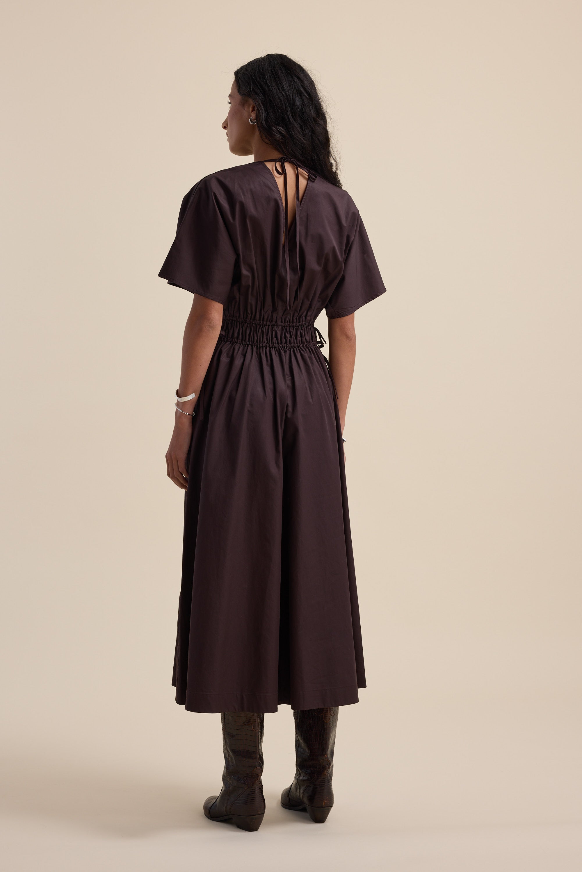 Woman in a Max Megan Tie Waist Dress and boots, standing with her back to the camera.