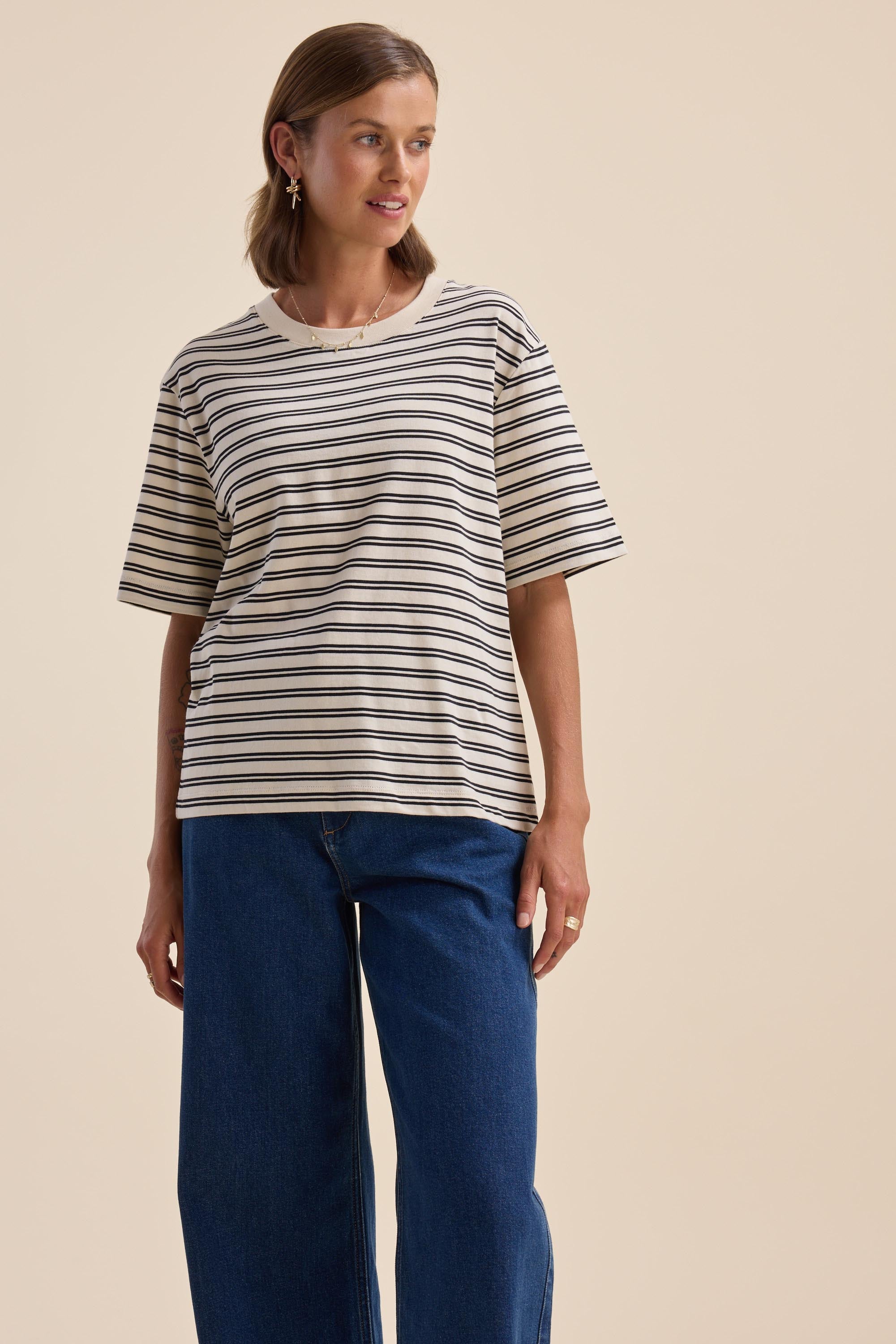 Woman wears Max Charmaine Organic/Pima Cotton Tee and blue jeans against a beige background.