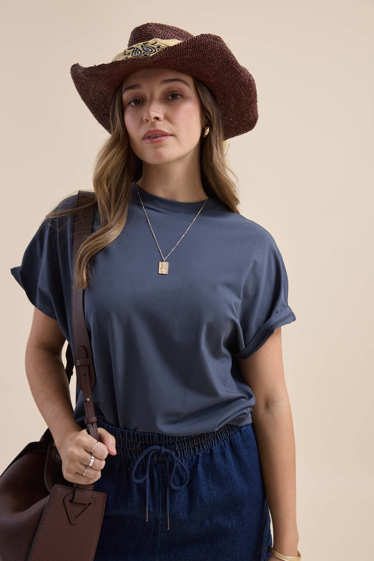 Woman in cowboy hat wears Elementary Slouchy Short Sleeve Tee, holding a brown bag, facing camera.