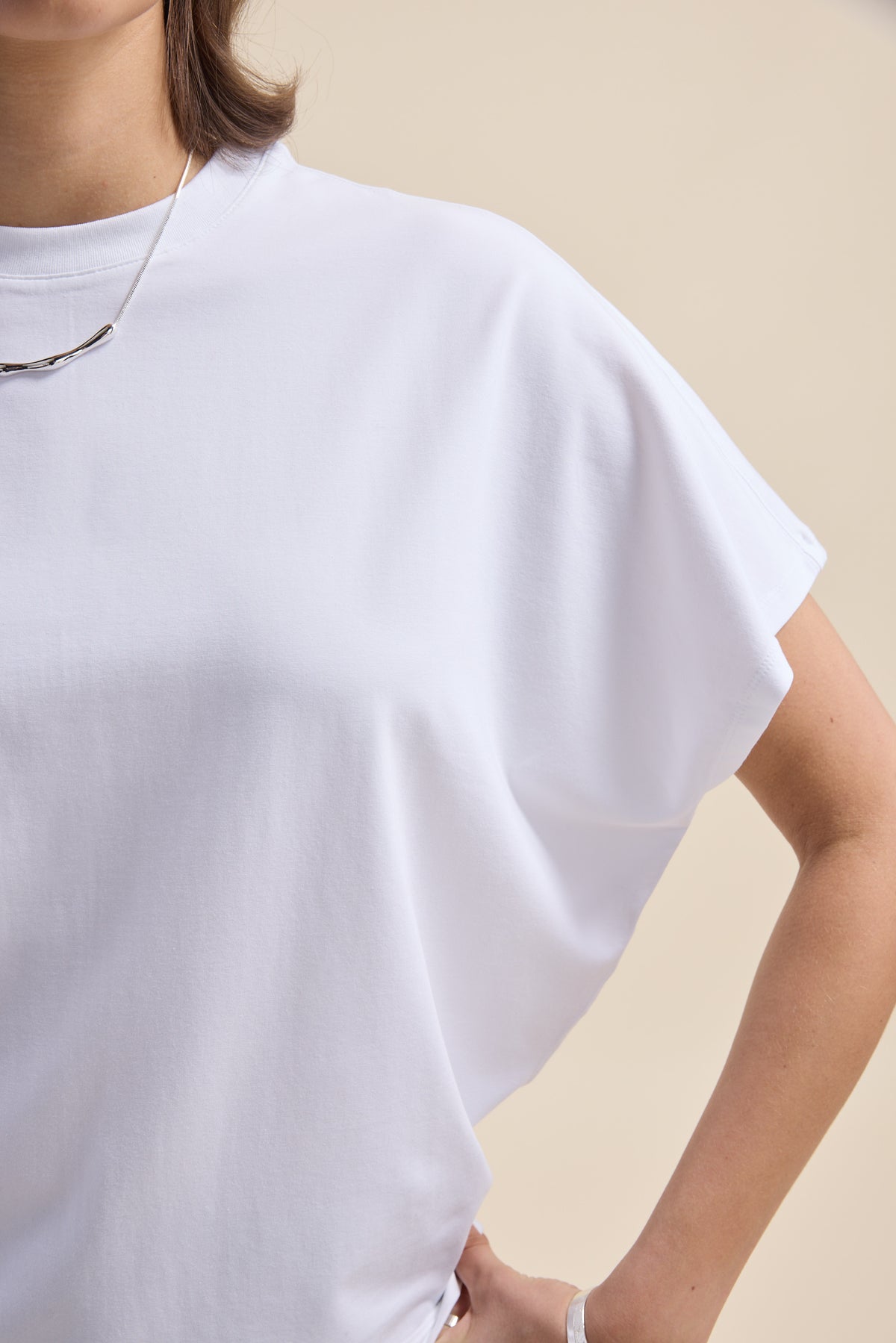 Person in an Elementary Slouchy Short Sleeve Tee, hand on hip, necklace, neutral background.