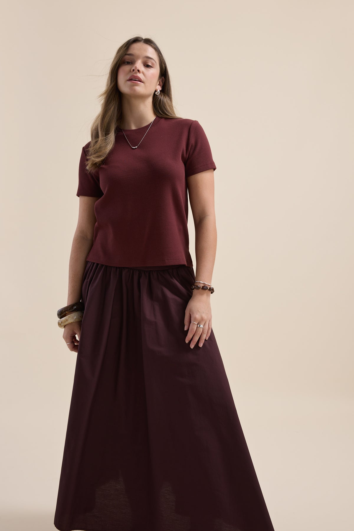 Woman in Elementary Ribbed Boxy Tee and long skirt stands against a plain beige background.