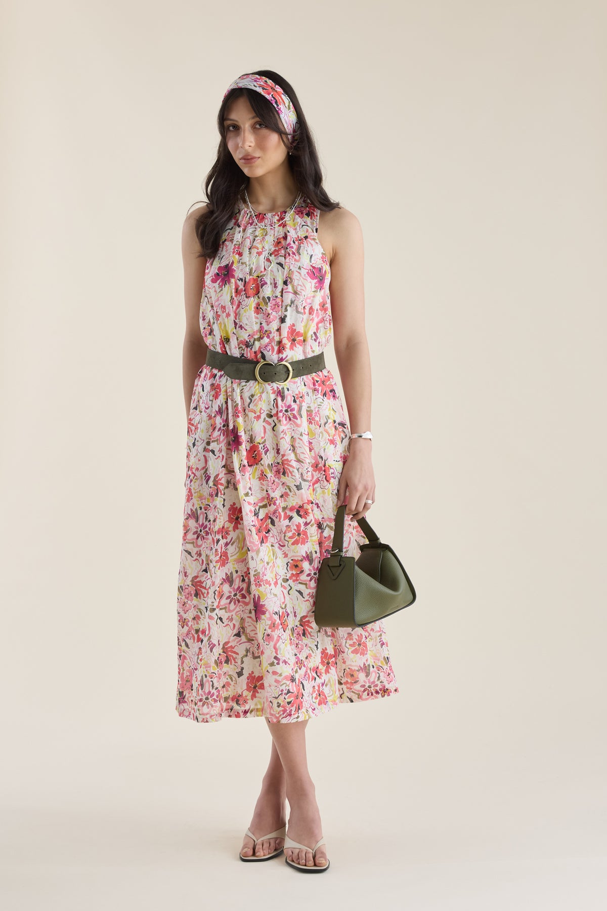 Woman in Max Kira Back Detail Dress and headband holds a green handbag on a neutral background.