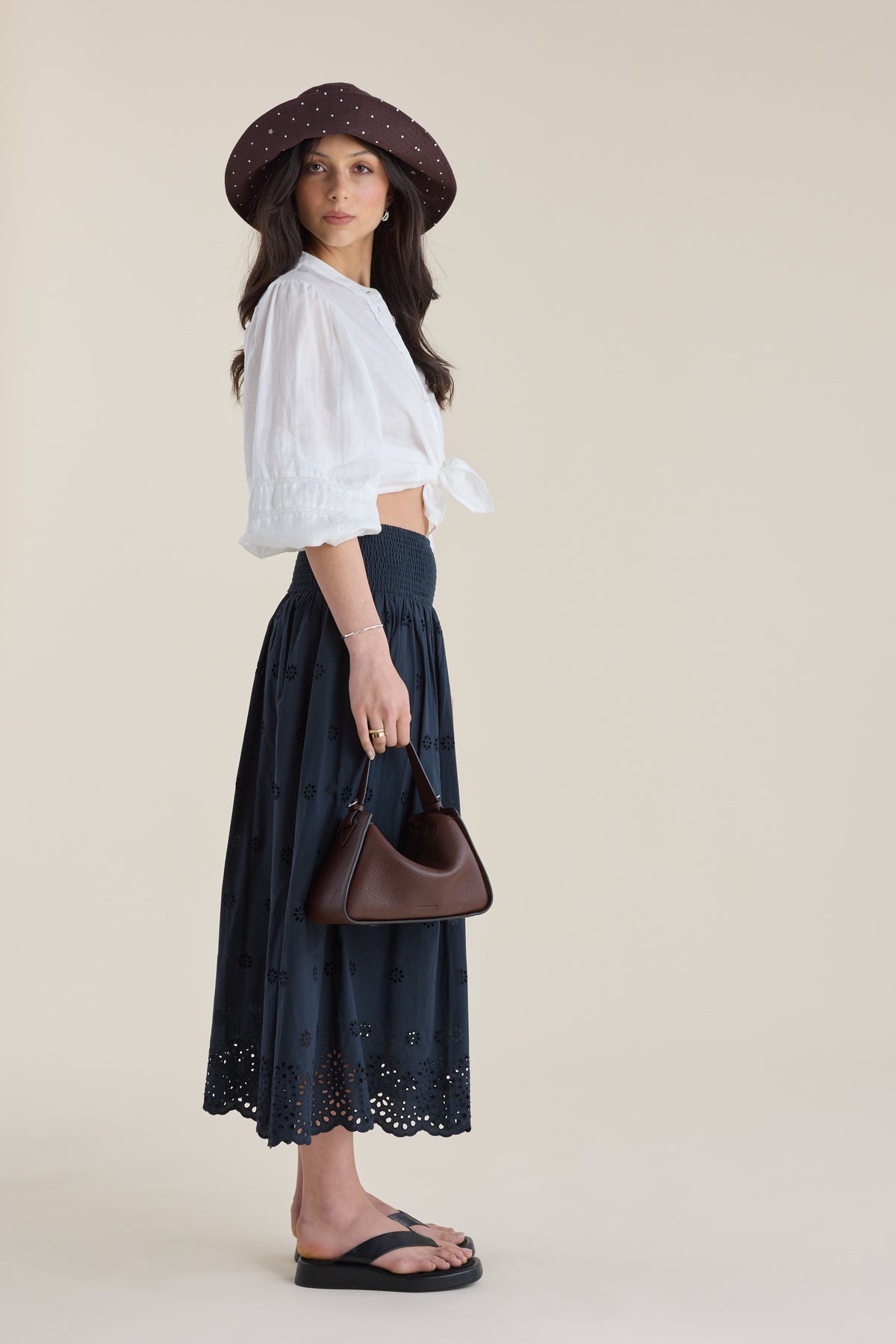 Woman in white blouse, Elementary skirt, and hat holds a small brown purse.