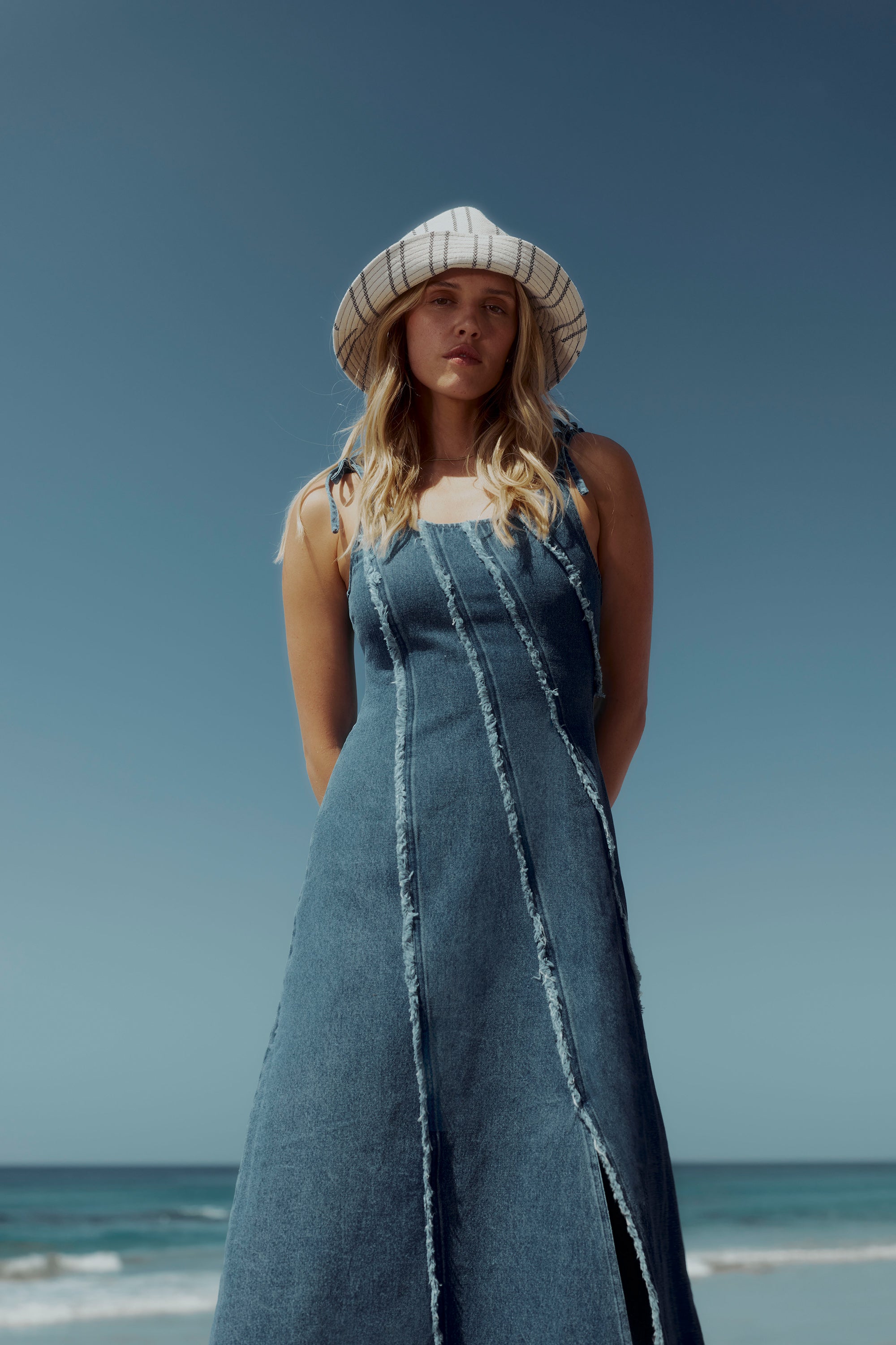 Woman wears the Max Rosa Denim Panel Detail Dress, standing on the beach by the ocean.