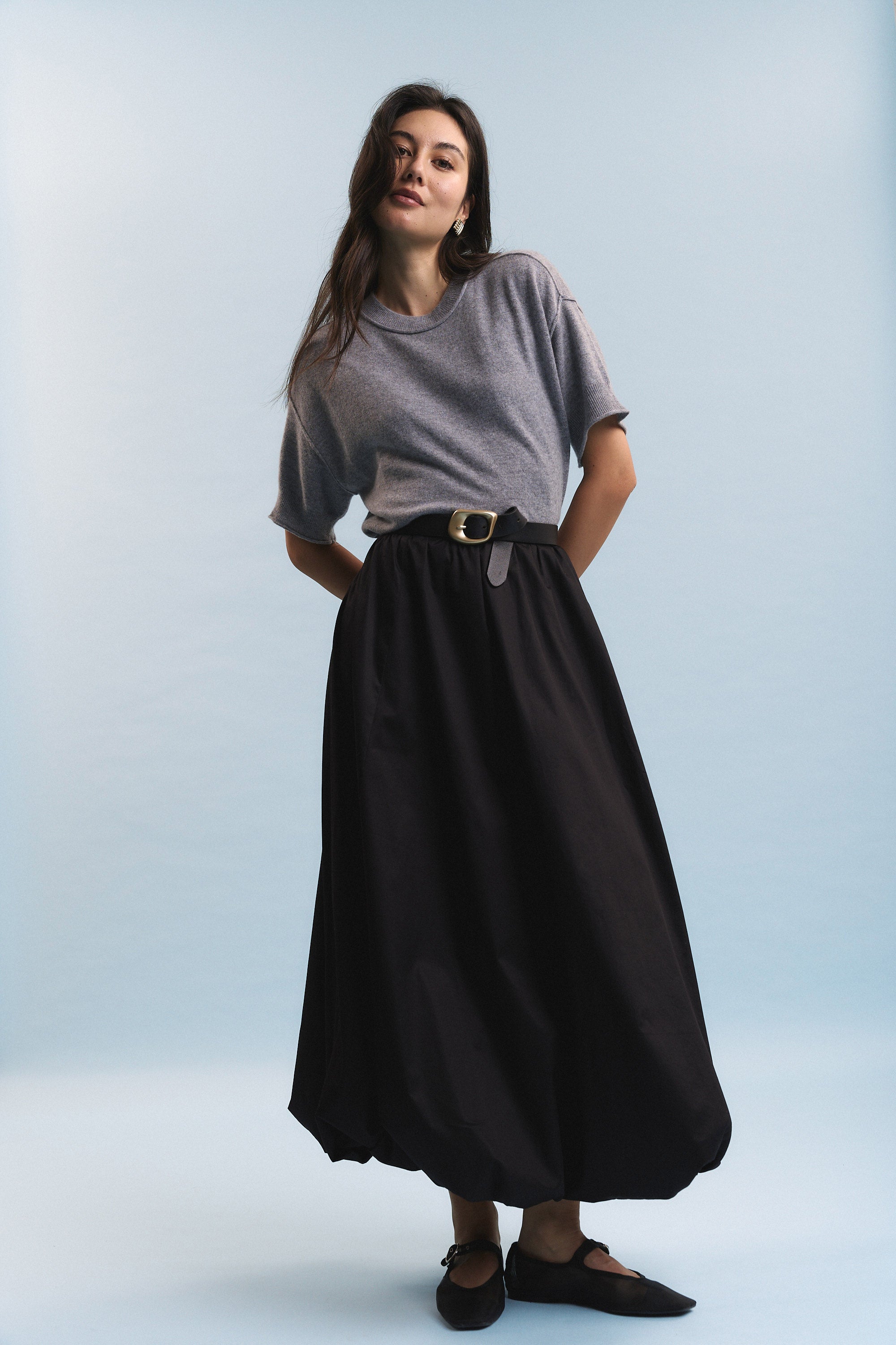 Woman in grey top and Max Juniper Bubble Hem Skirt poses against light blue background.