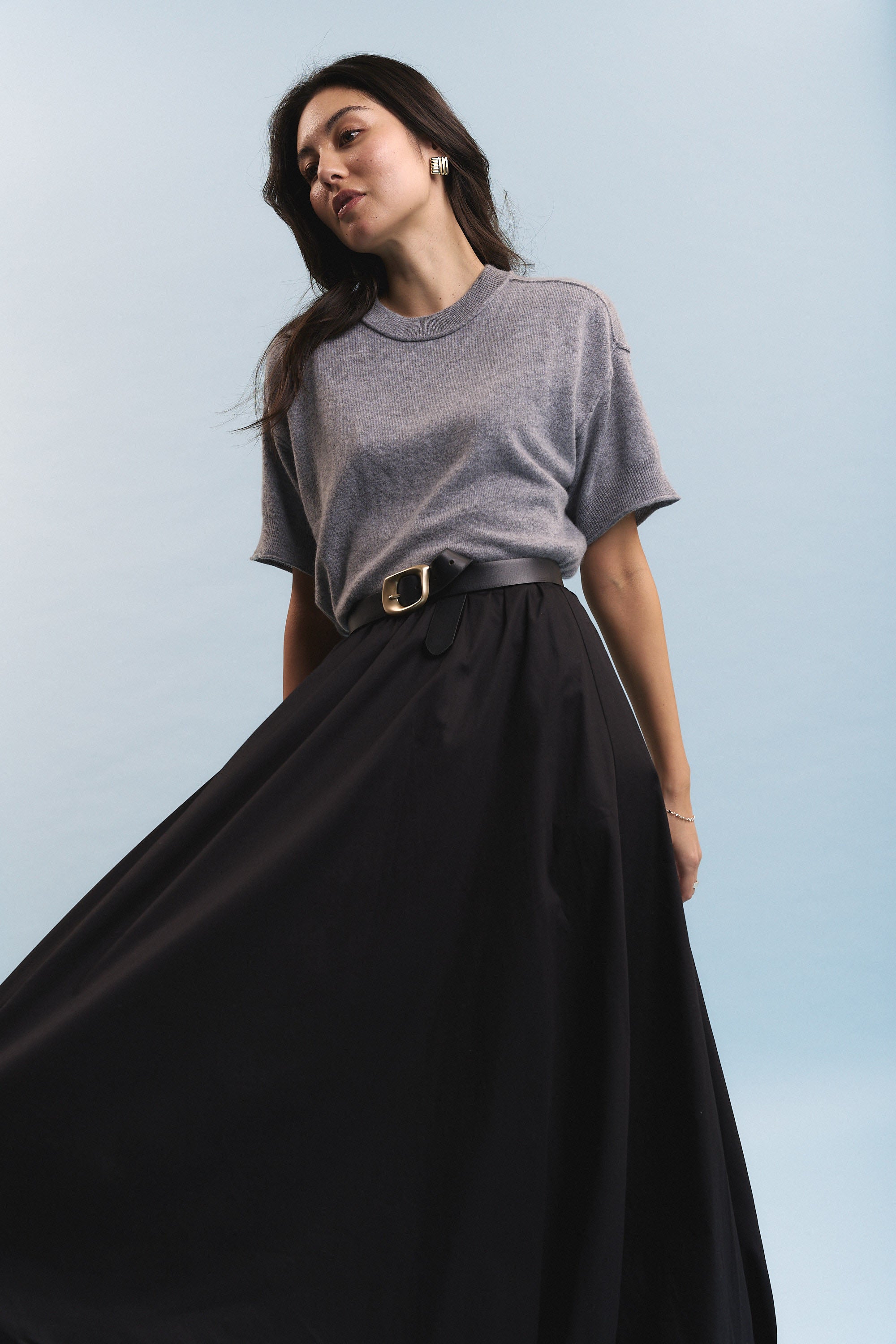Woman in grey tee and Max Juniper Bubble Hem Skirt poses by a light blue background.