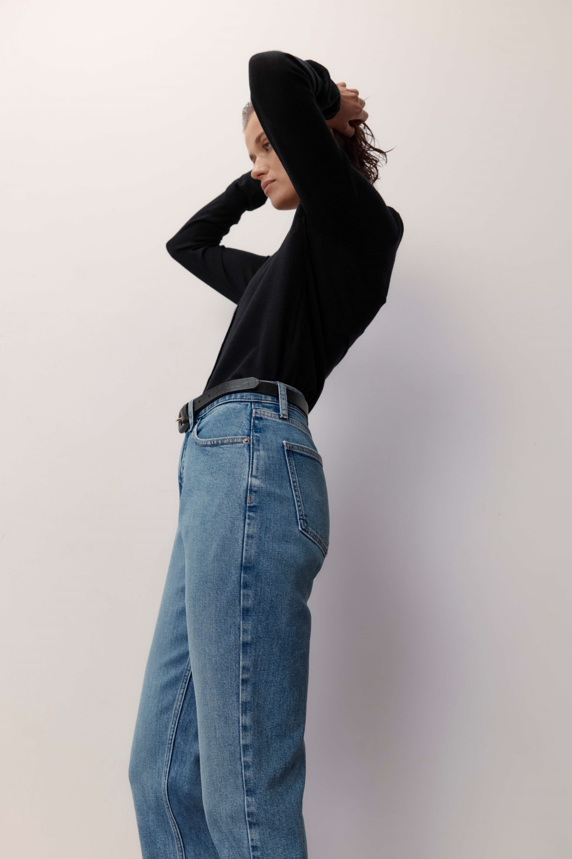 Model in a black long-sleeve shirt and Max Georgia Slim Jeans stands sideways against a light background.