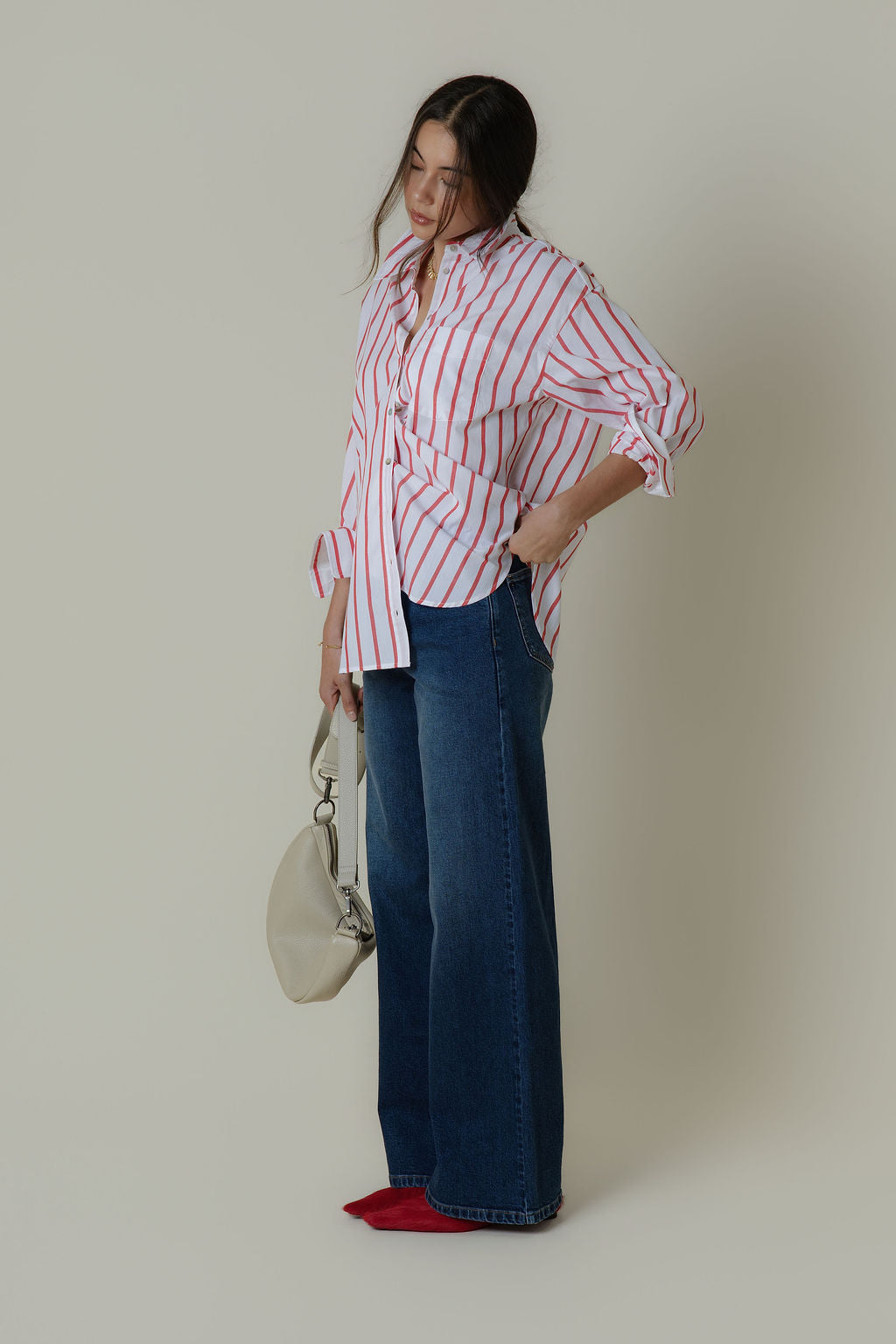 Woman in striped shirt and Max Nevada Wide jeans, holding cream bag by a plain wall.