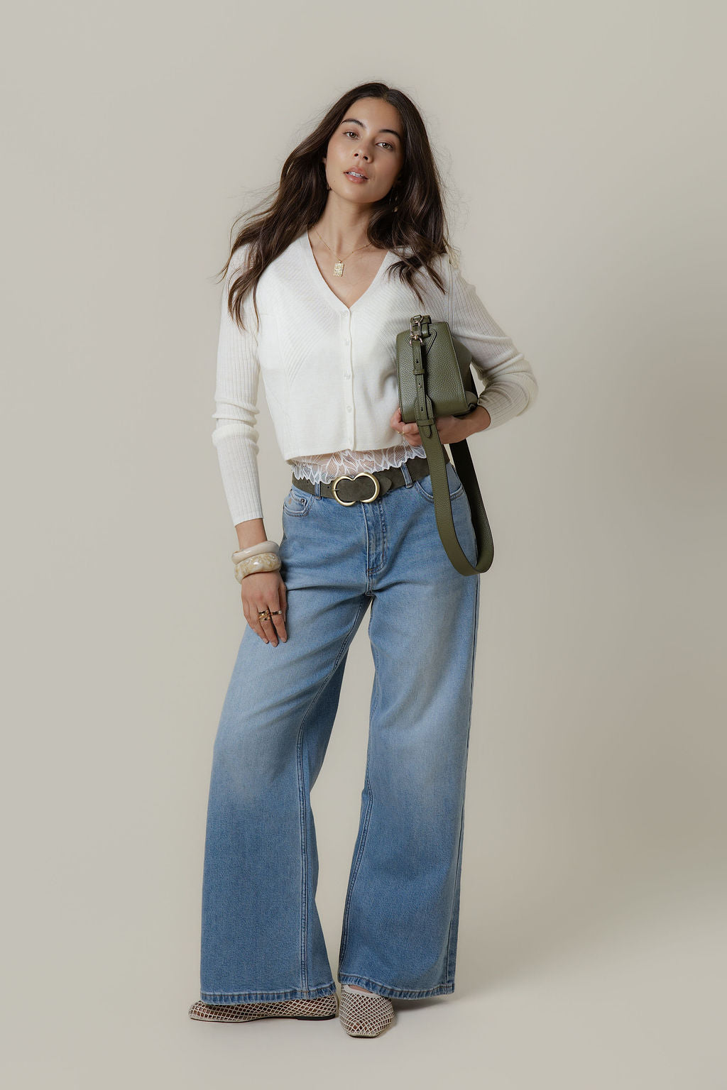 Woman in The Mid Rise Wide Leg Jean by Max, white cardigan, green handbag, plain background.