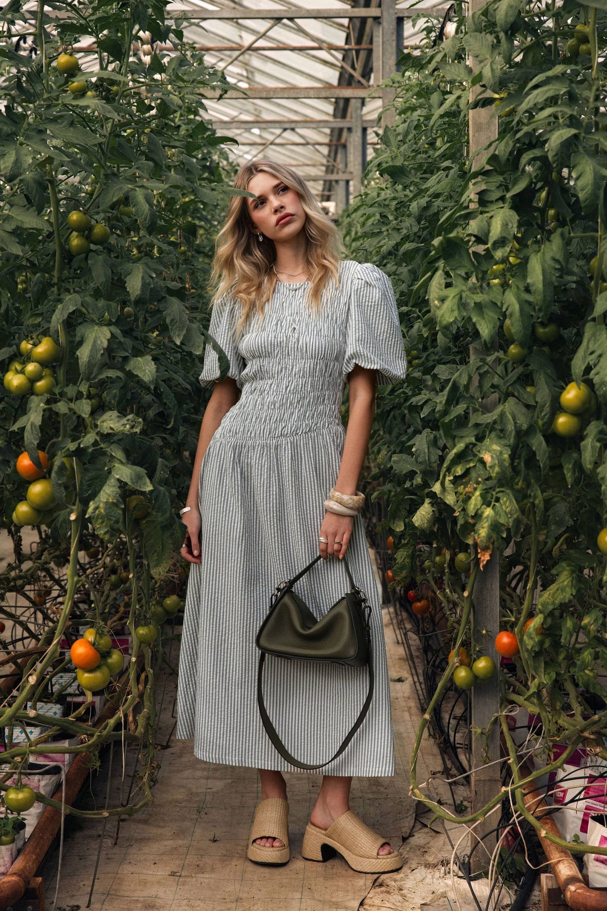 Woman in Max Talia Shirred Detail Midi Dress holds green bag in greenhouse.