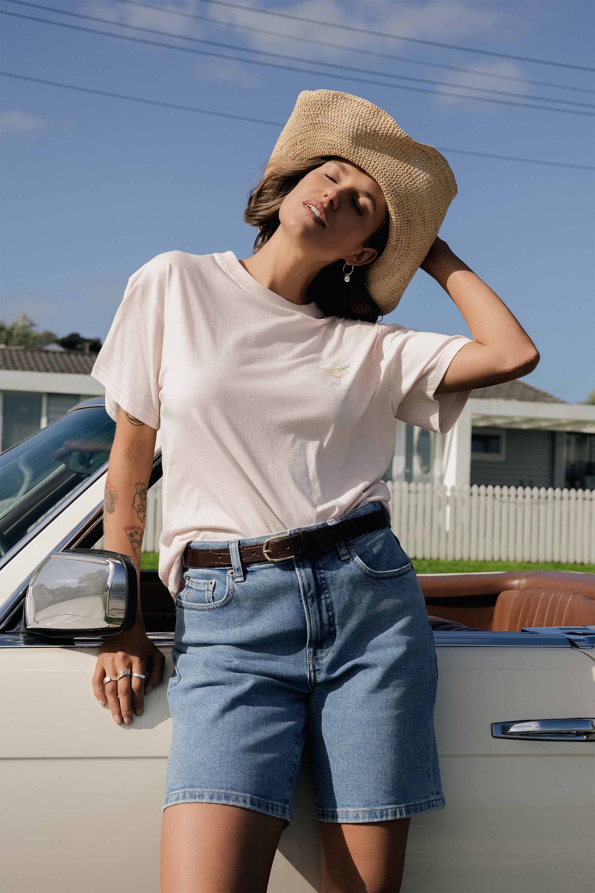 Woman in The Classic Denim Short by Max leans on a white convertible under a blue sky.