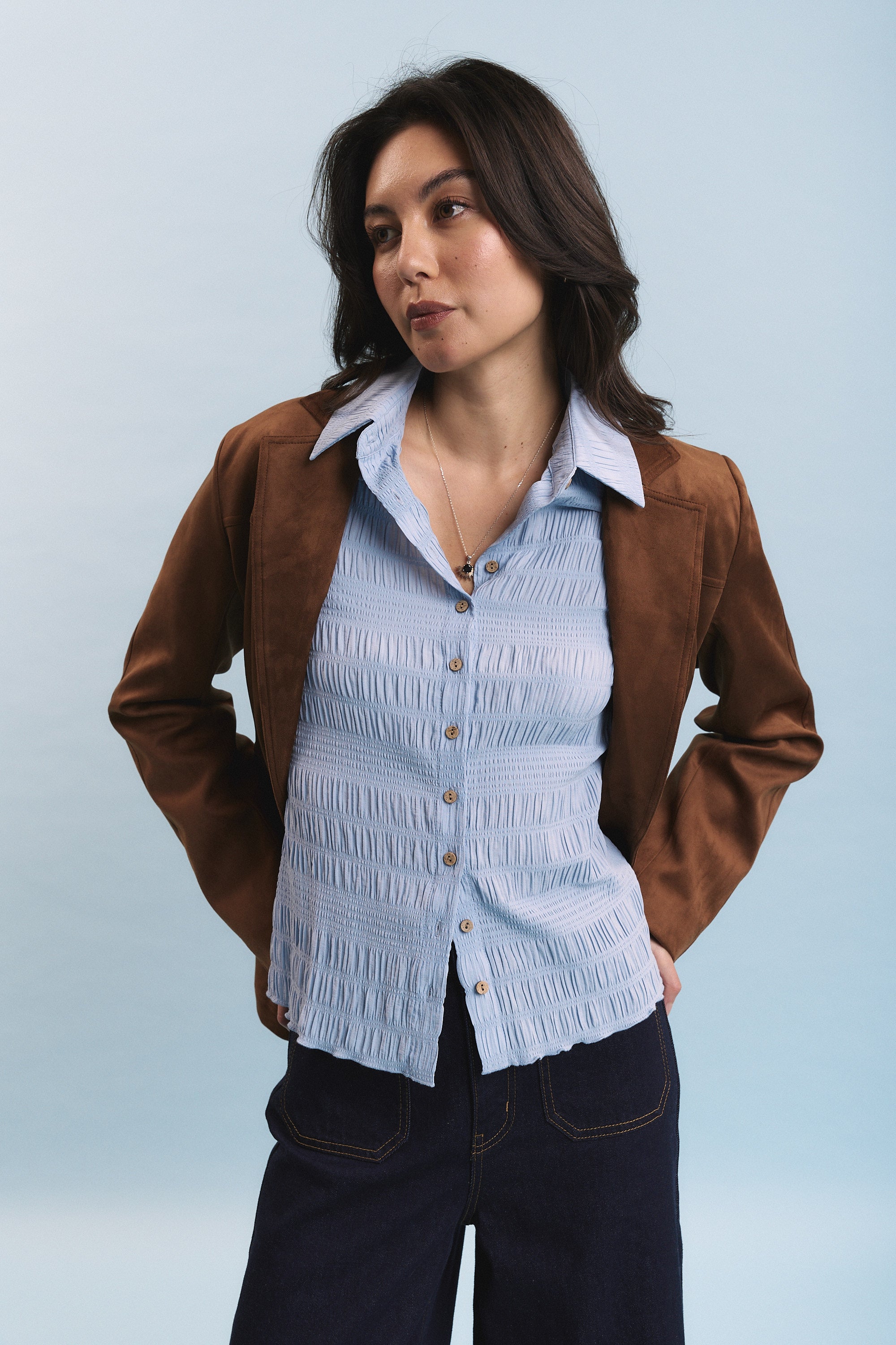 Woman in a Max Tahlia Shirred Detail Shirt and brown jacket against a light blue background.