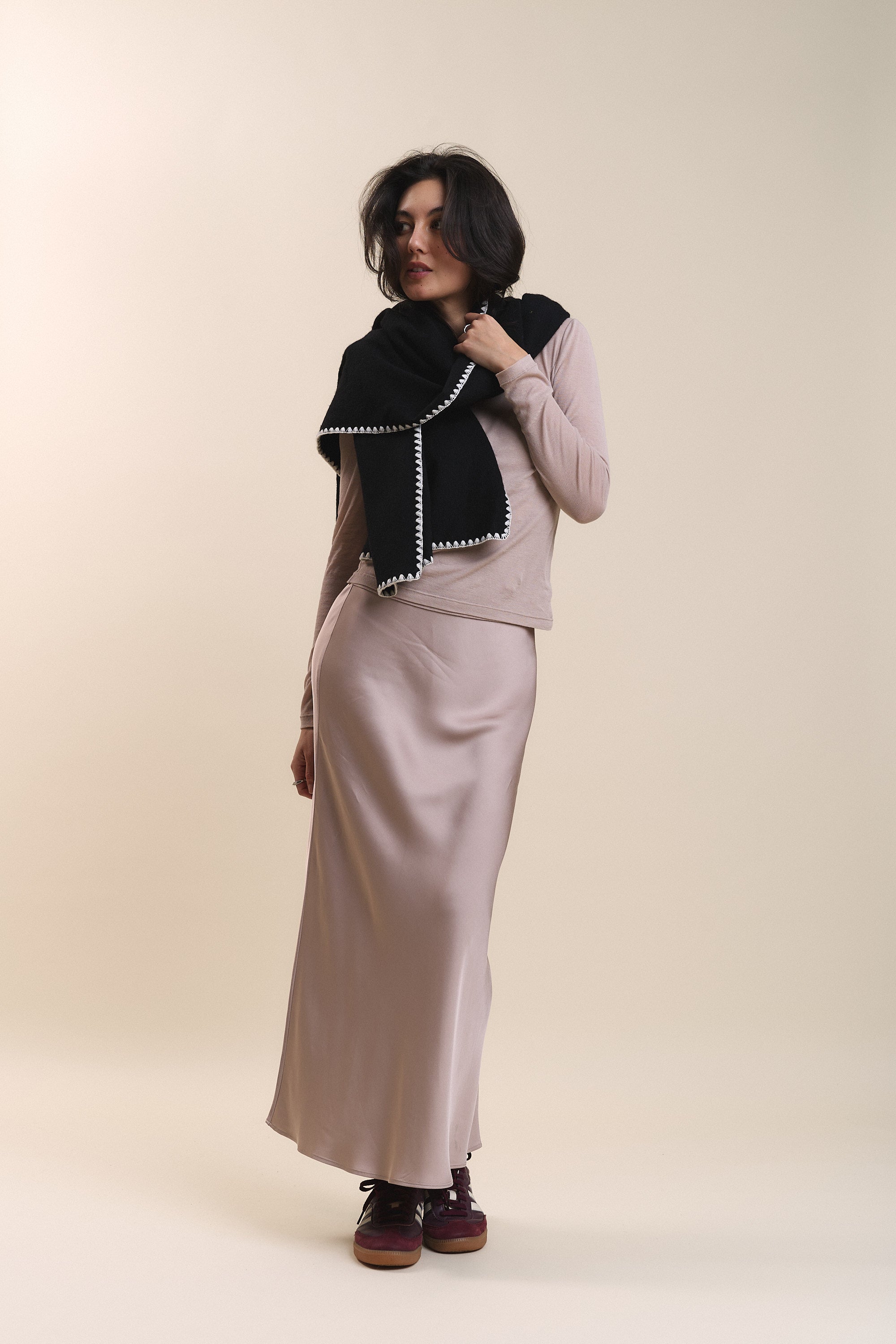 Woman in Max's Holly Slip Skirt, sweater, black shawl, and sneakers poses by a beige background.