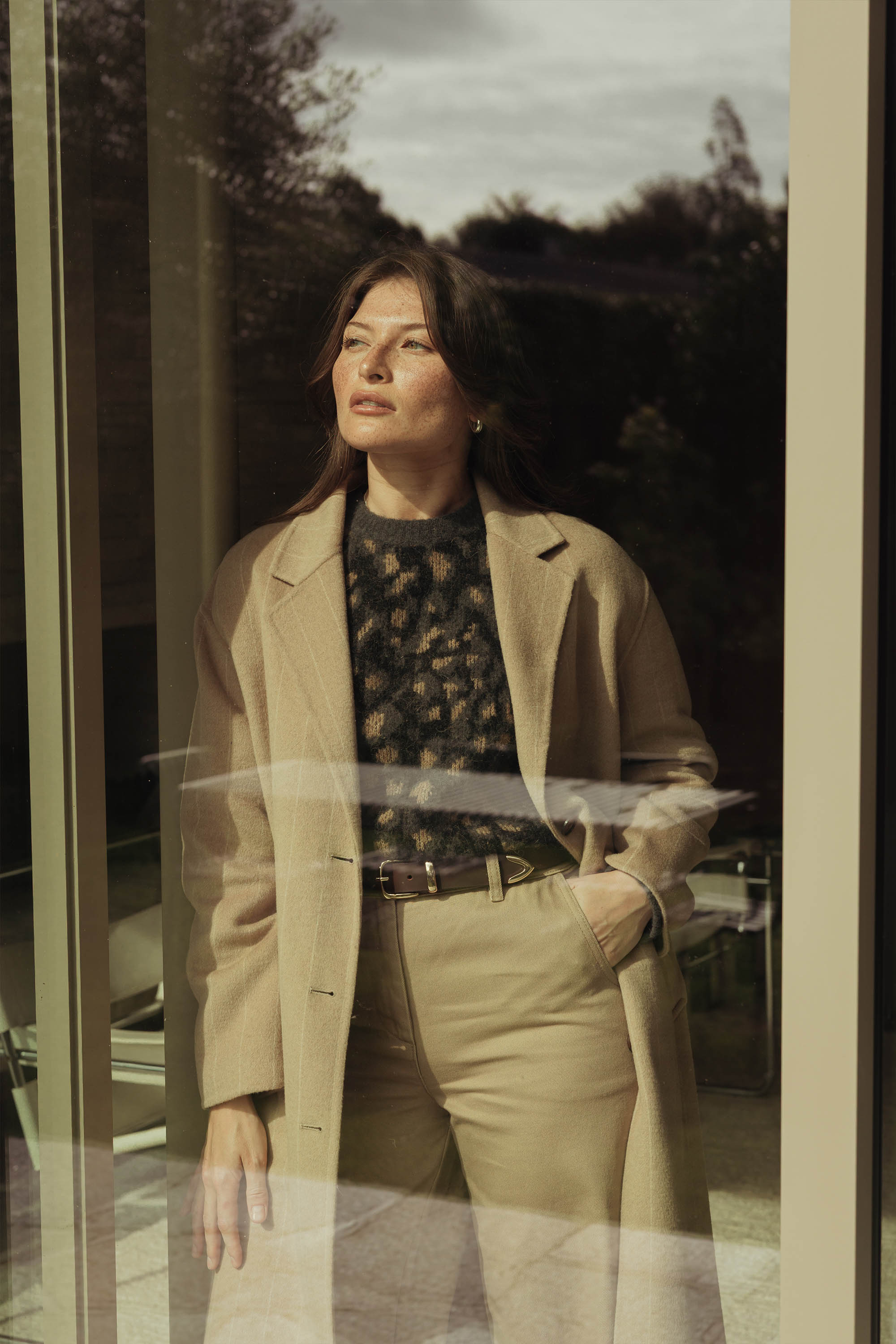 A woman in a Max Hayley Luxe Whisper Crew Neck Sweater stands indoors, looking outside.