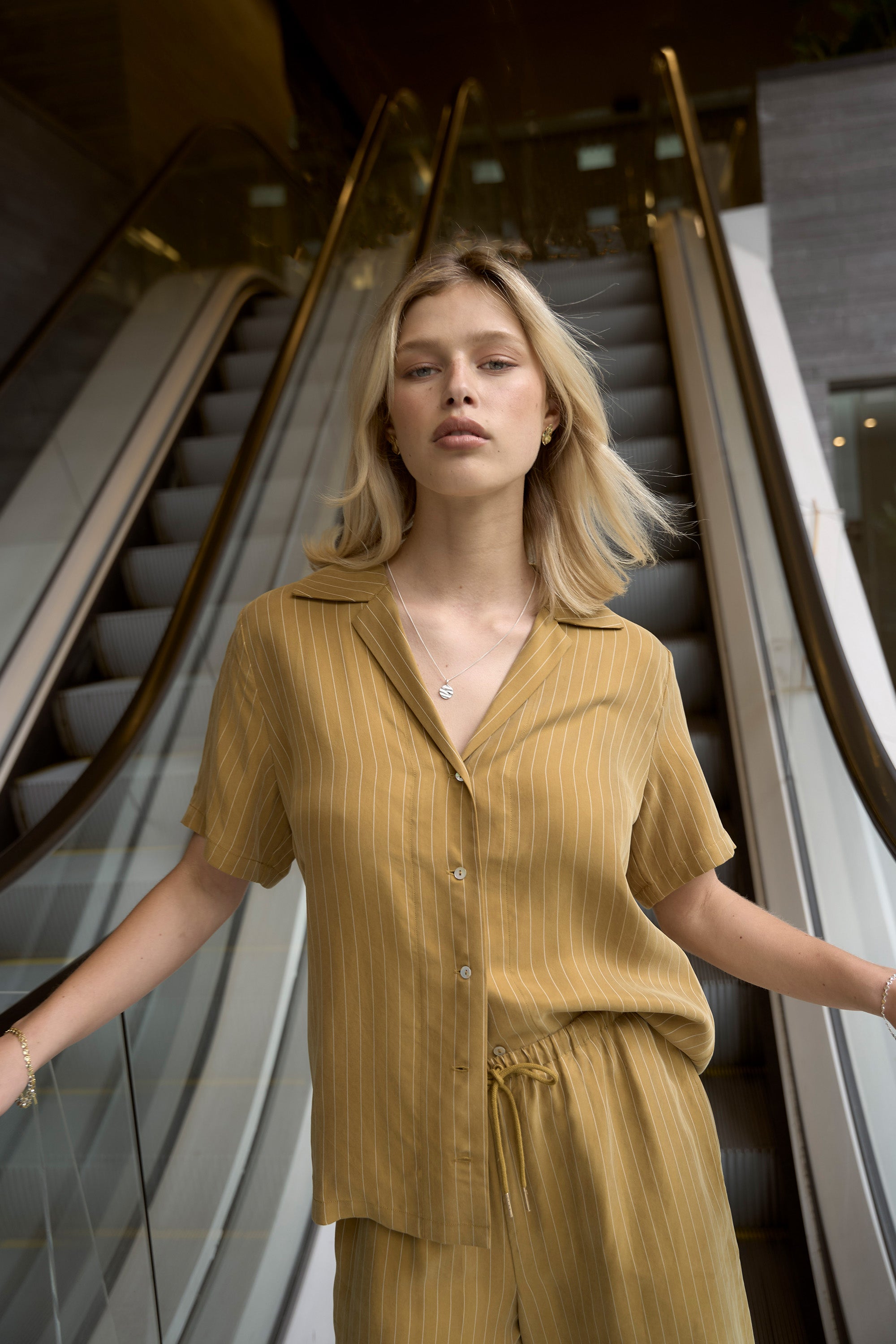 Woman in the Max Amy Short Sleeve Shirt stands confidently by the escalator.