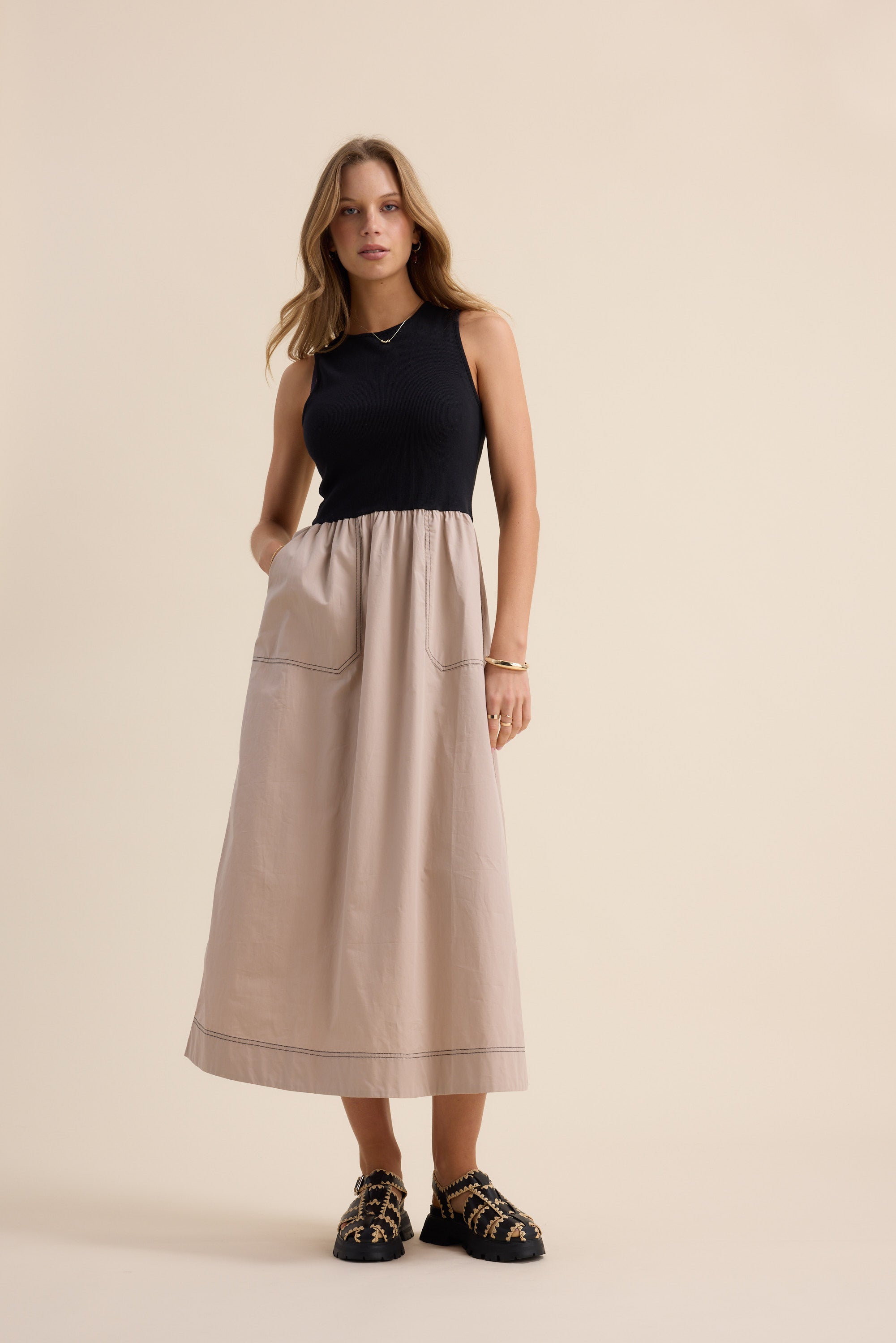 Woman wears The Stitch Detail Dress by Max, sleeveless black top and beige poplin skirt.