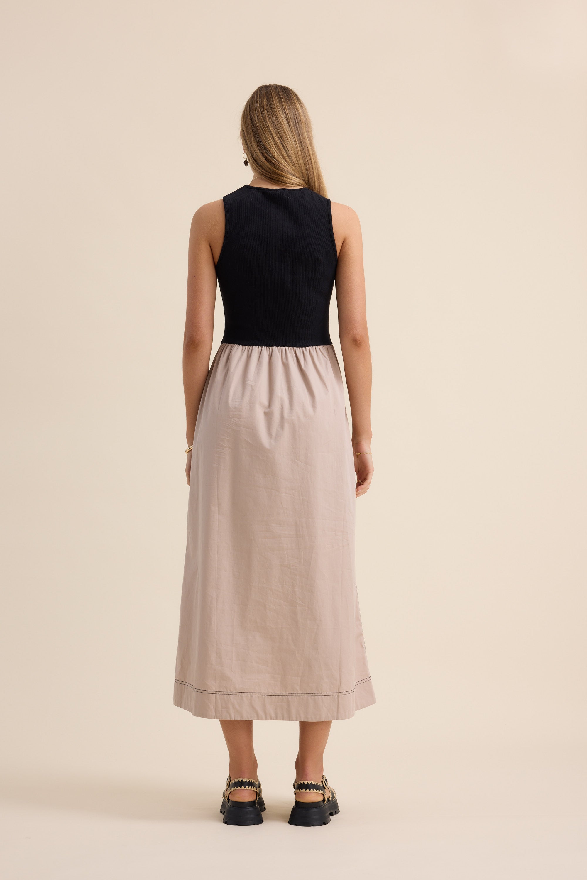Woman in The Stitch Detail Dress by Max, sleeveless black and beige, stands on plain background.