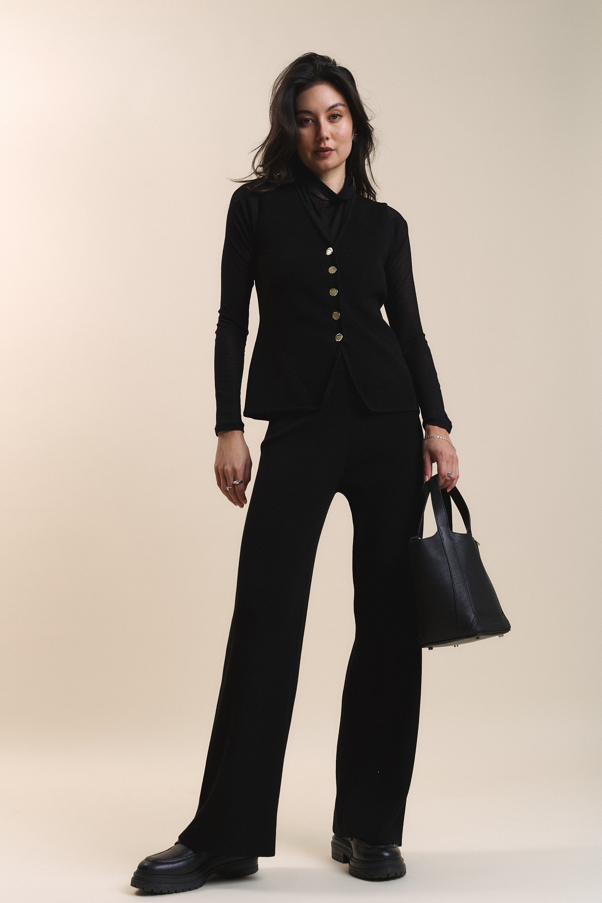 Woman in Charlie Knitted Pants by Max, holding a black bag against a beige background.