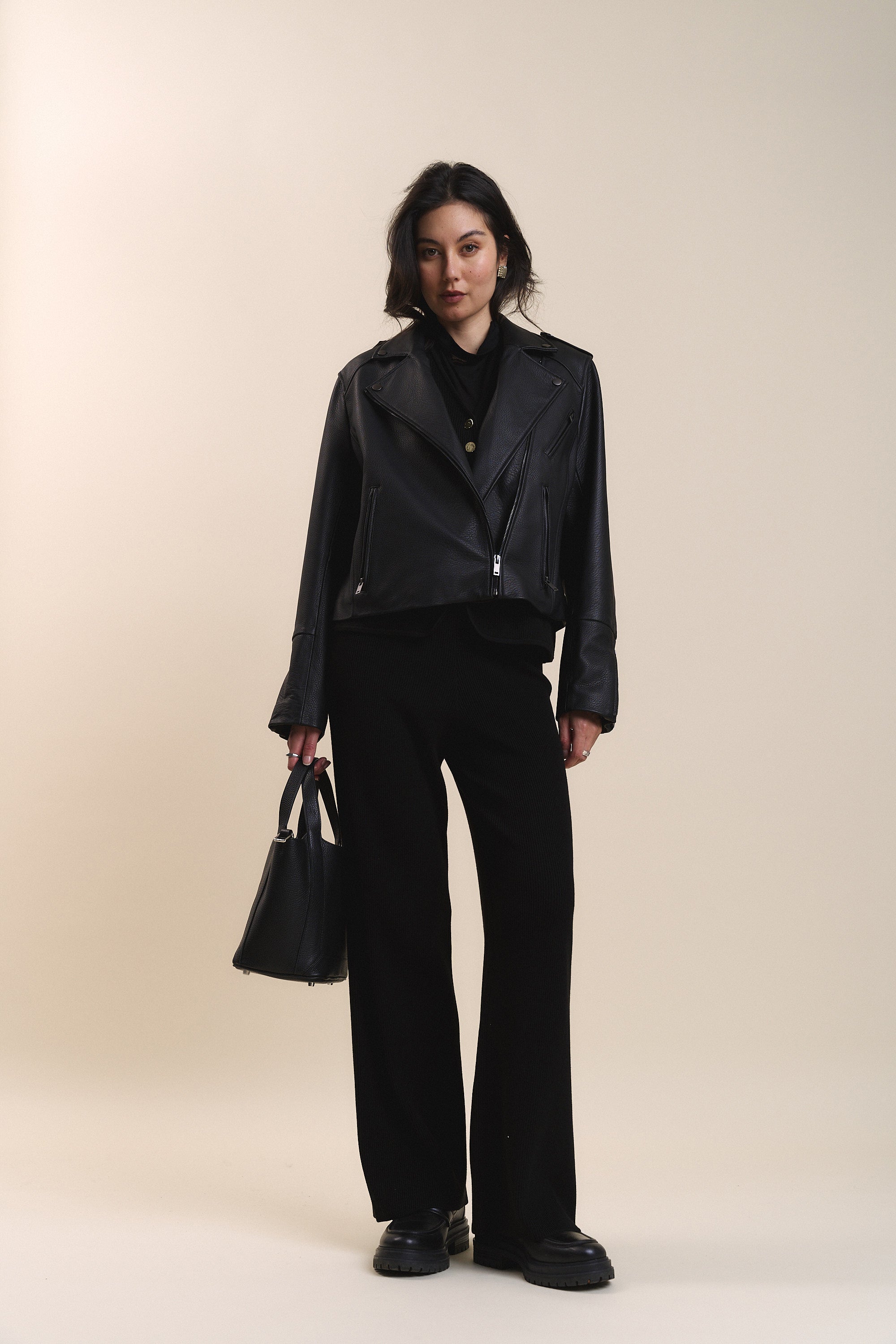 Woman wearing Max Charlie Knitted Pants and jacket, holding a handbag against a plain background.