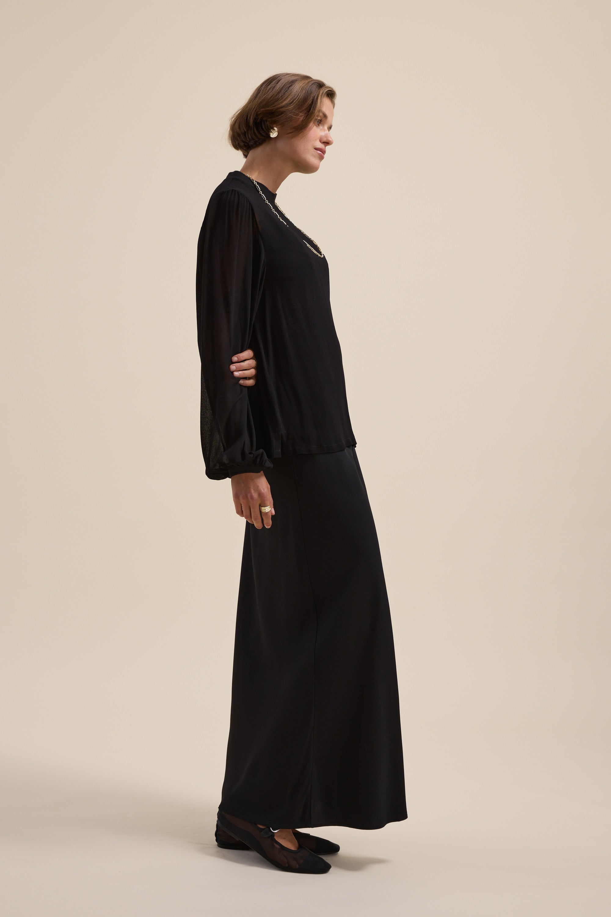 Woman wears the Max Maxi Slip Skirt and blouse, standing sideways against a beige background.