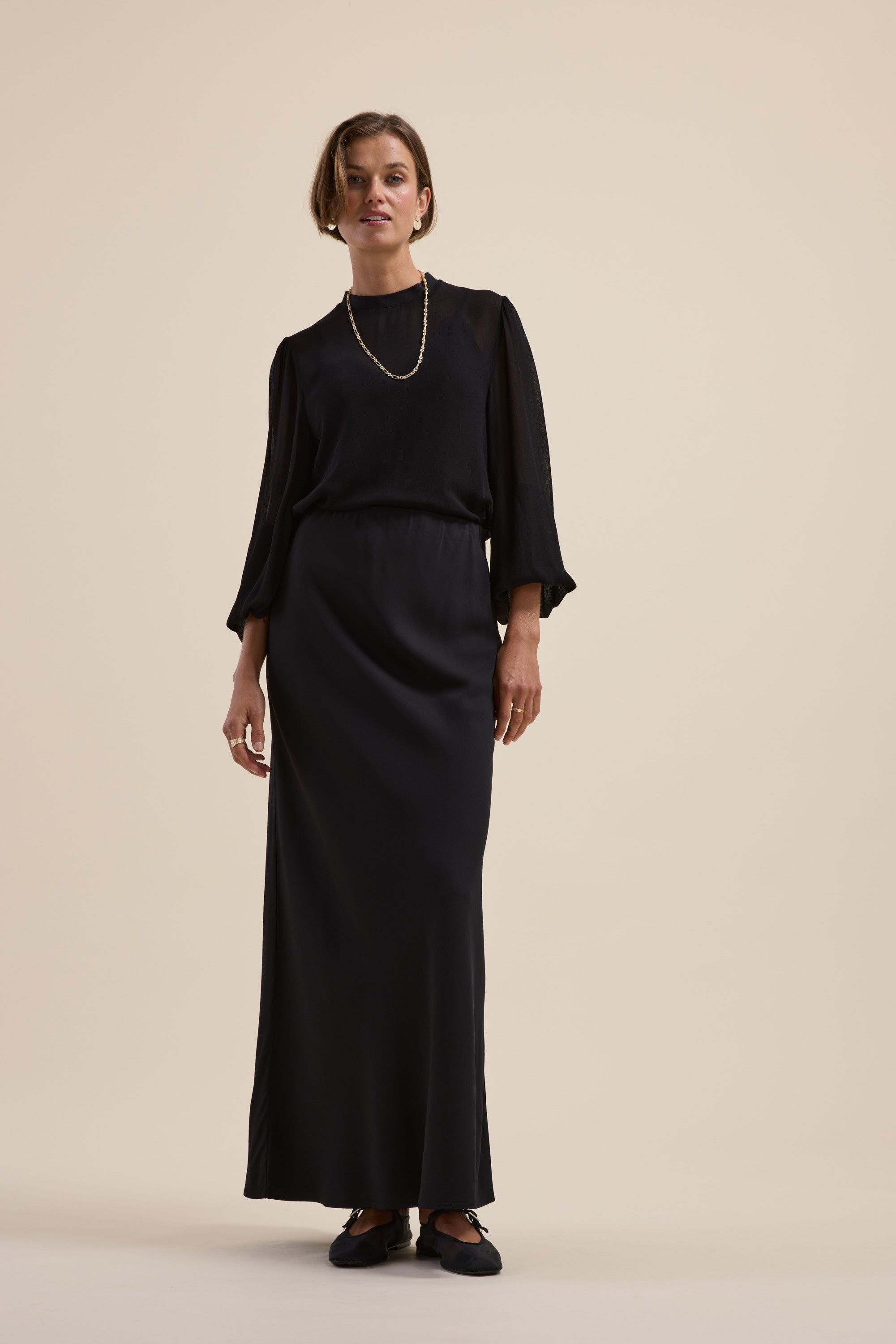 A woman in Max's The Maxi Slip Skirt stands against a plain beige background.