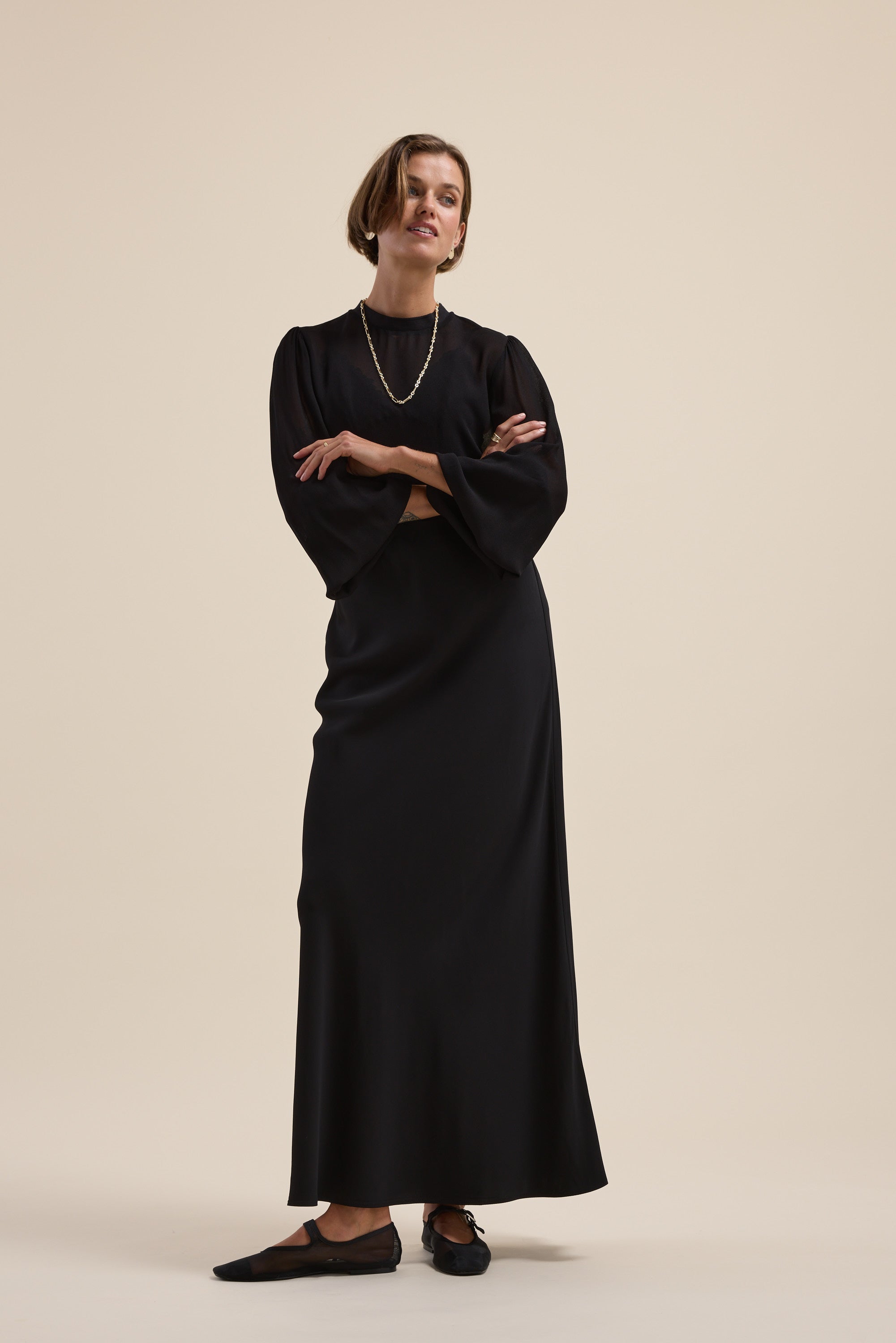 Woman in The Maxi Slip Skirt by Max, arms crossed, on a beige background.