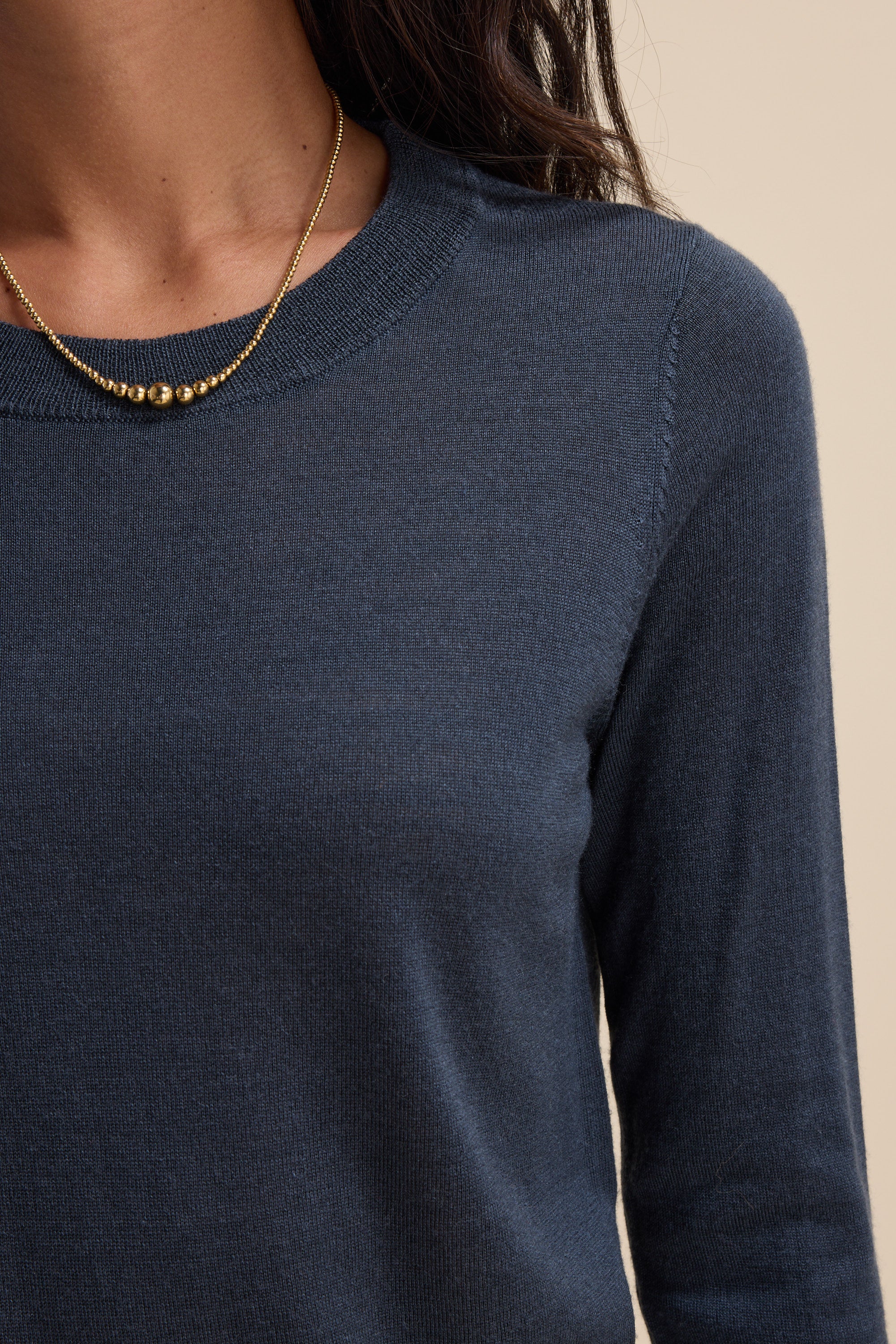 A woman in Max’s The Merino Silk Layering Top (navy) and a gold beaded necklace.