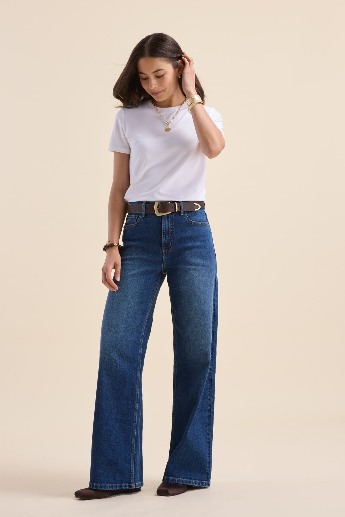 Woman in white tee and Max Nevada Wide jeans stands against beige backdrop, looking down.