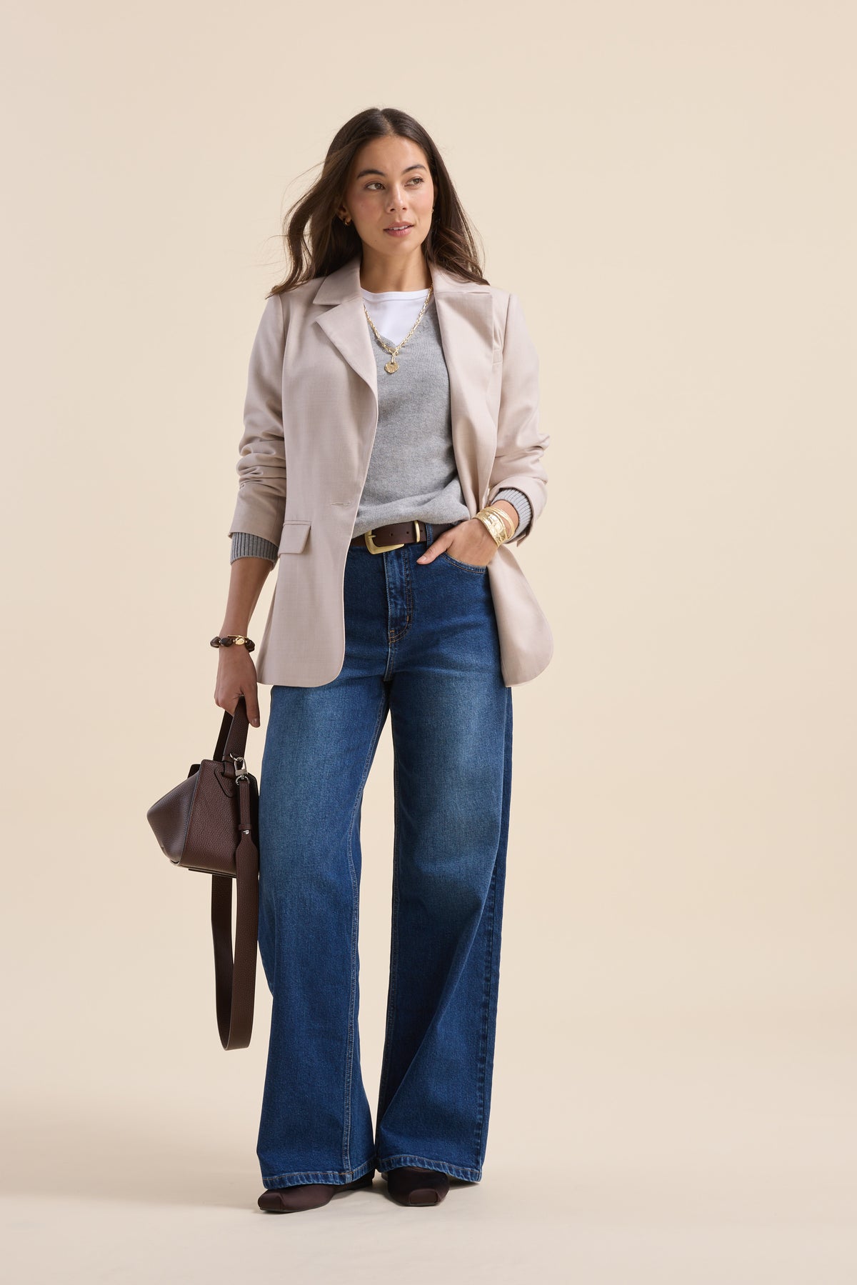 Woman in Max Nevada Wide jeans, gray blazer, brown handbag, on a beige background.