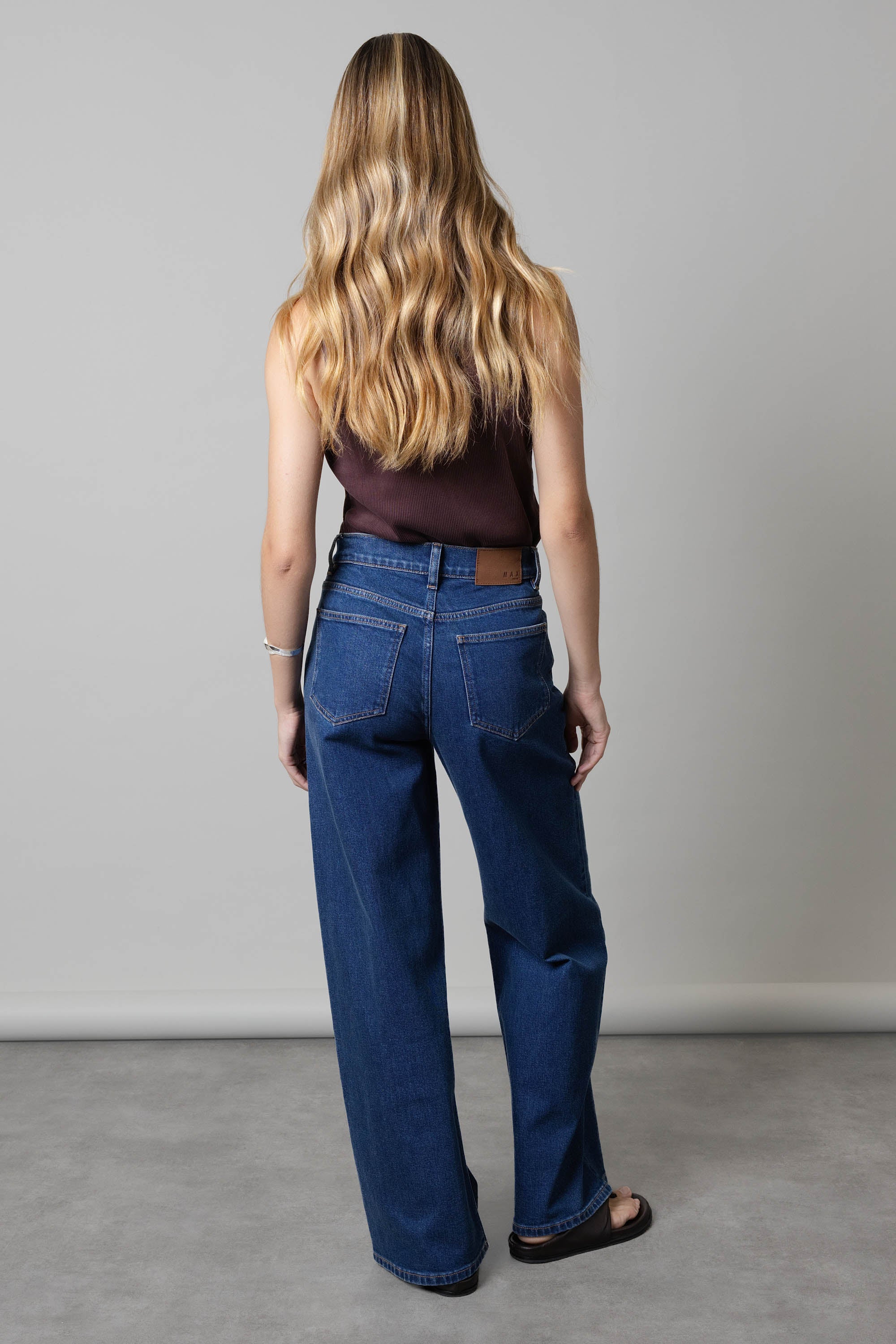 Woman with long wavy hair wears Max Nevada Wide Jeans and a dark top, back facing.