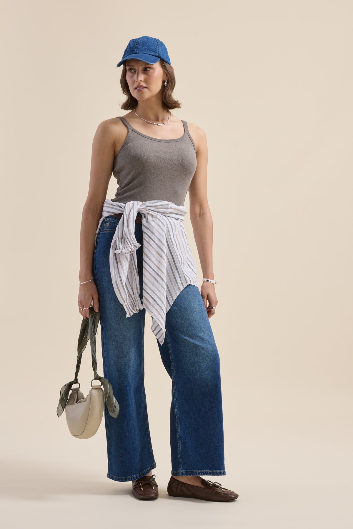Woman in Elementary Basics Rib Cami by Elementary, wide jeans, blue cap, striped shirt at waist.