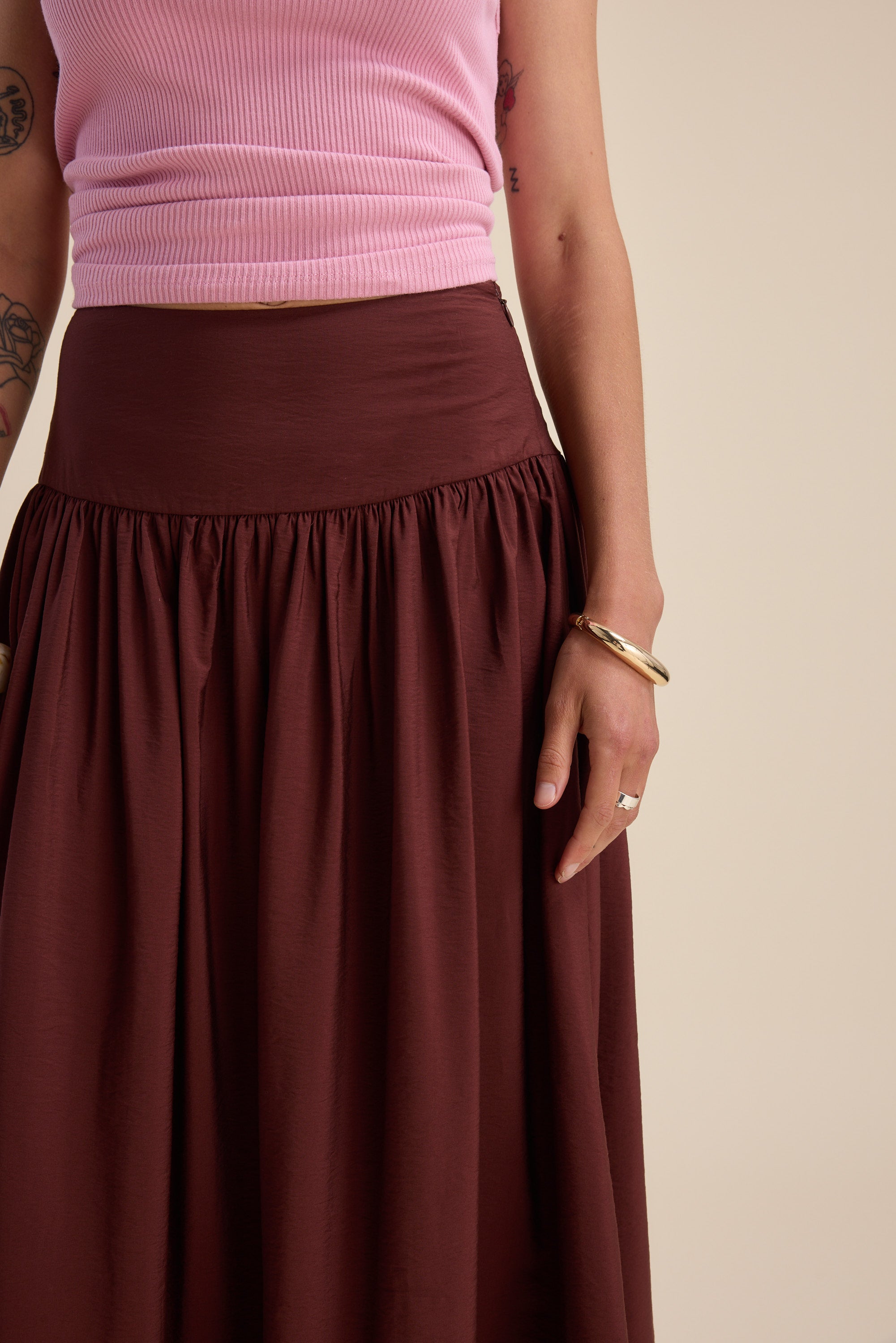 Person in Max’s Carrie Tiered Skirt and pink ribbed top, accessorized with bracelets and tattoos.