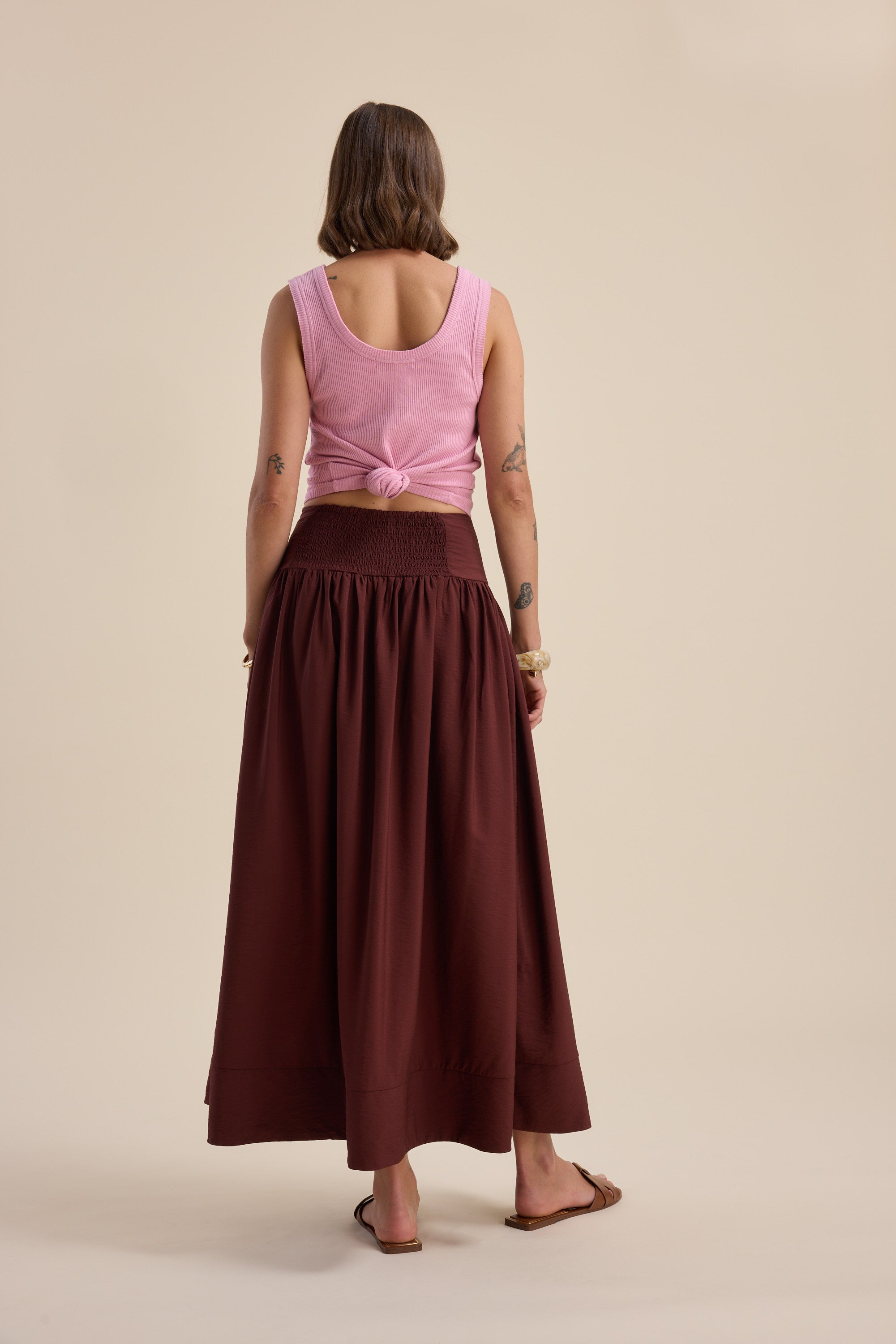 Woman in a pink tank and Max Carrie Tiered Skirt stands barefoot, facing away from camera.