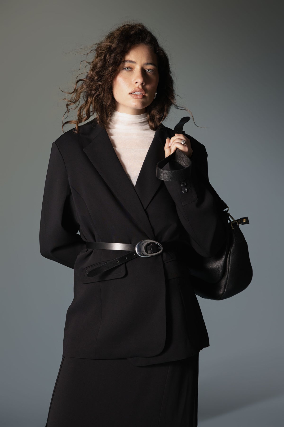 Woman in Max Sheer Layering Top, black blazer & skirt, with handbag, looks at camera.
