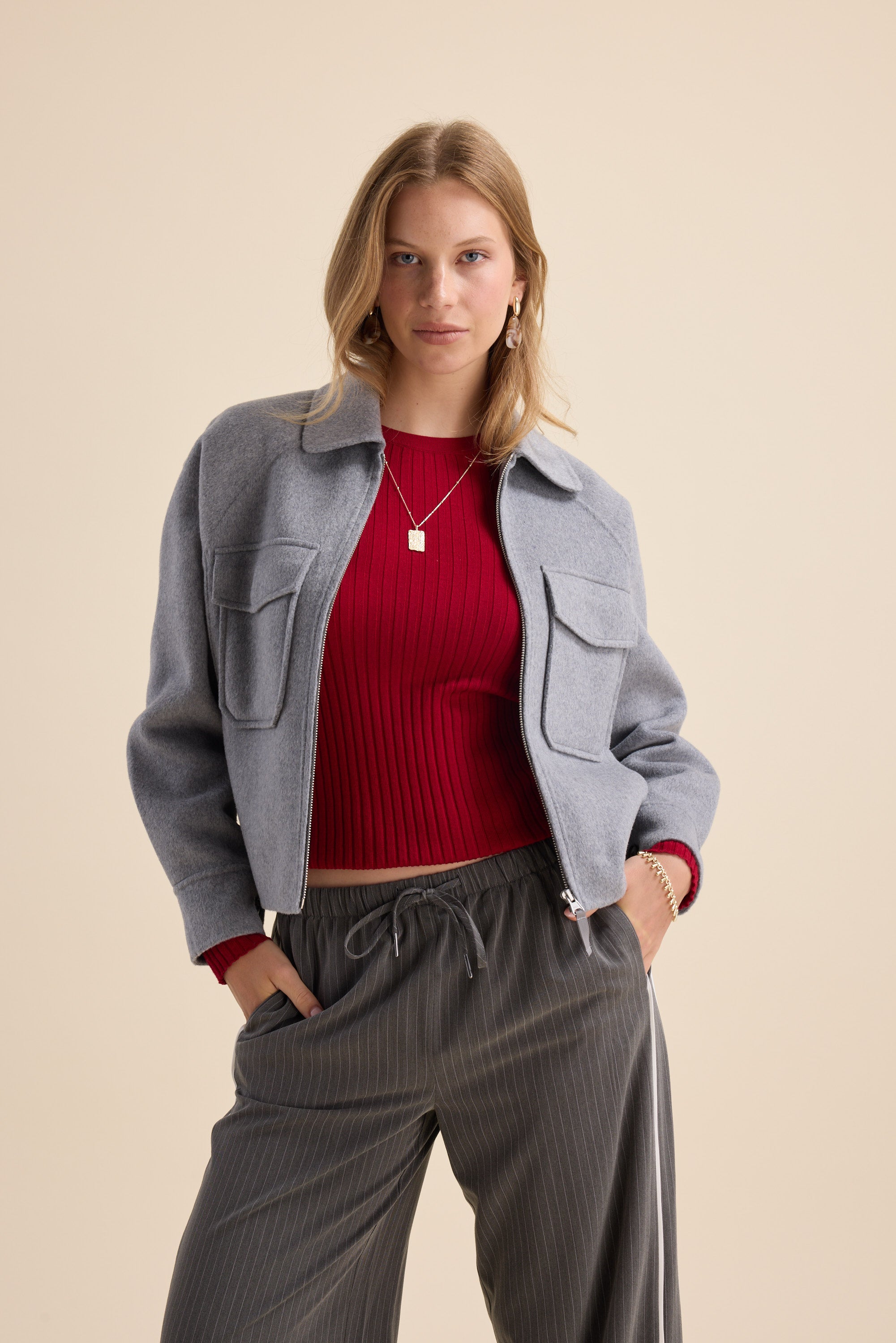 Woman in Max's Zip Front Wool Blend Cropped Coat, red ribbed sweater, and gray pants.