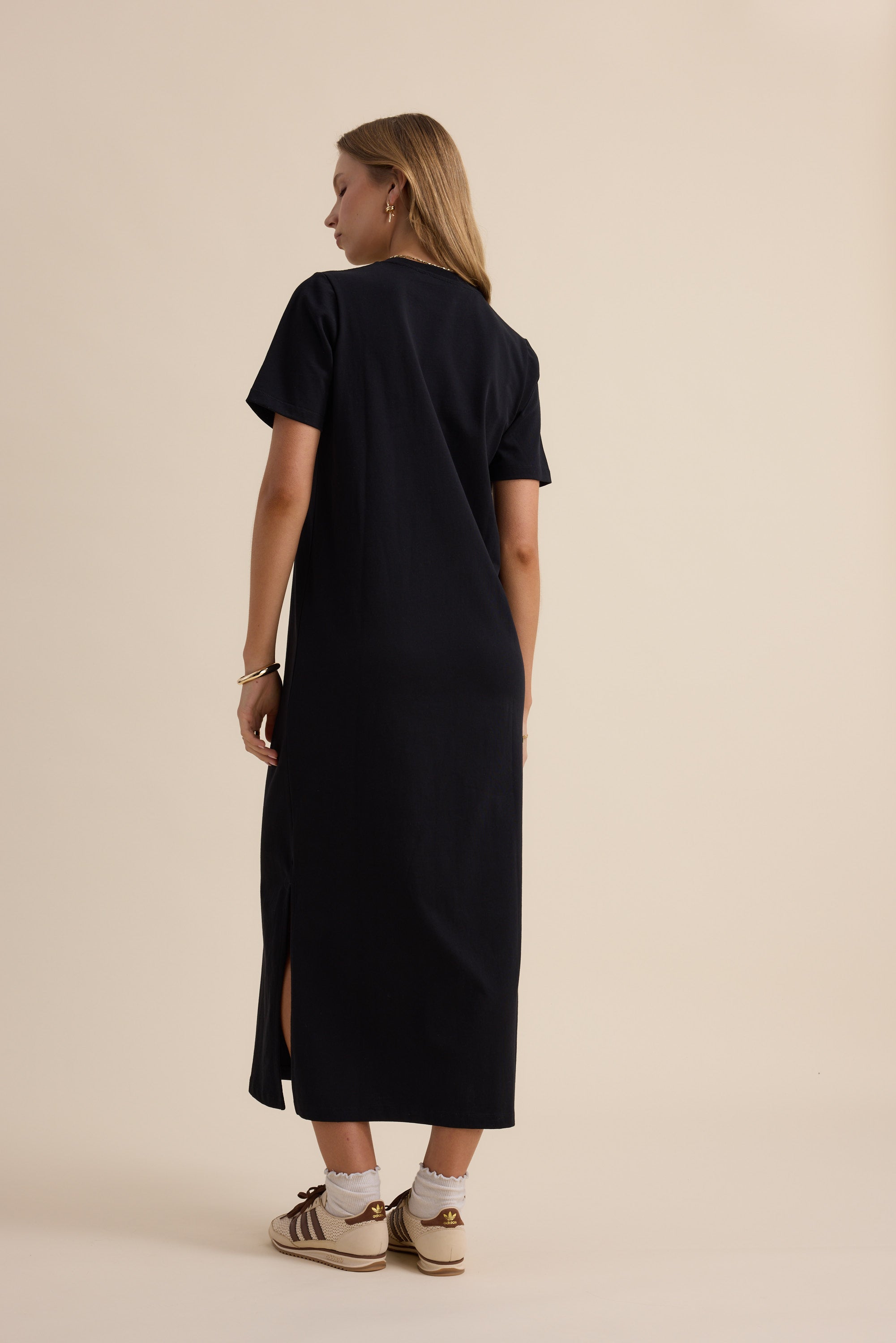 Woman in Max's The Tee Shirt Dress, black, facing away, paired with sneakers.