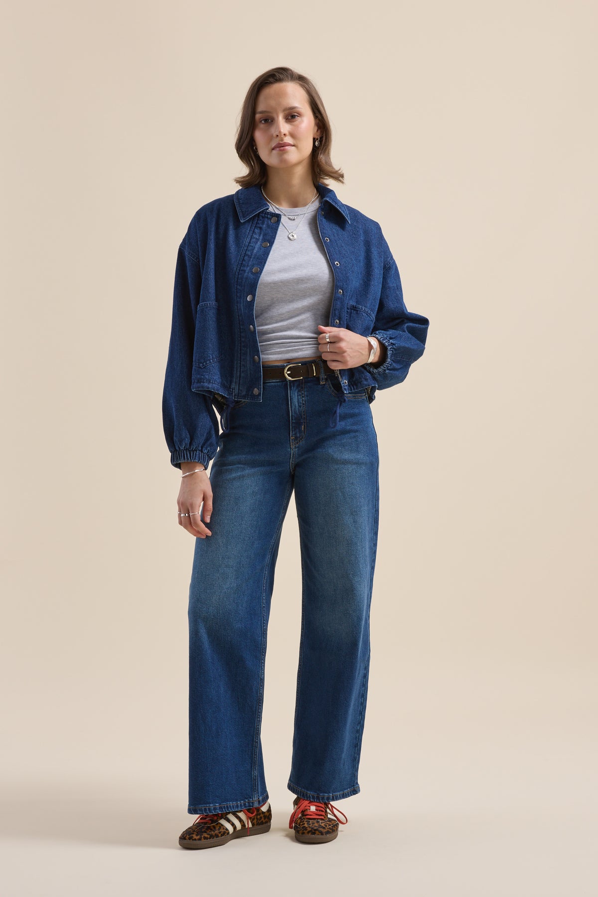 Woman in Elementary Relaxed Jacket, gray shirt, blue jeans, and patterned shoes facing forward.