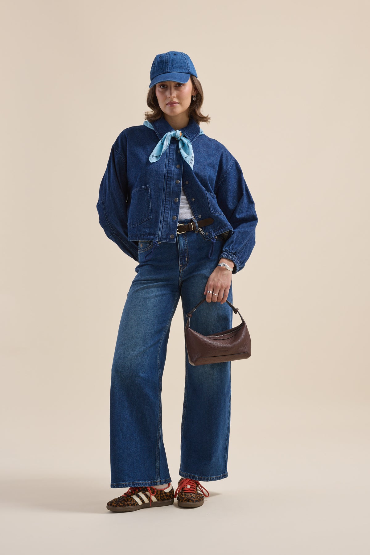 Woman in Elementary Relaxed Jacket, wide jeans, blue cap, turquoise scarf, and small purse.