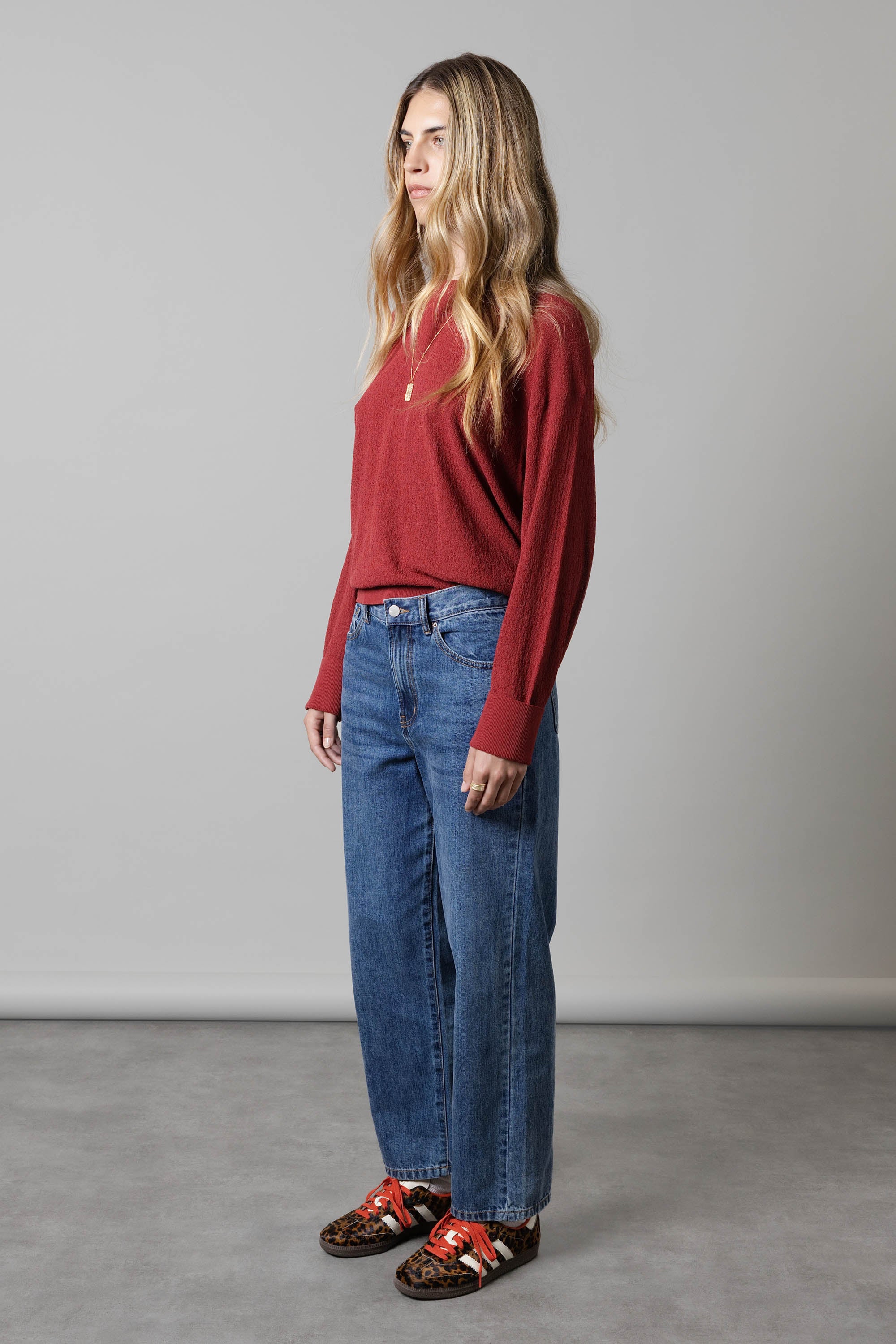 Woman in a red sweater, Max Borrowed From The Boys Jeans, and leopard sneakers in a studio.
