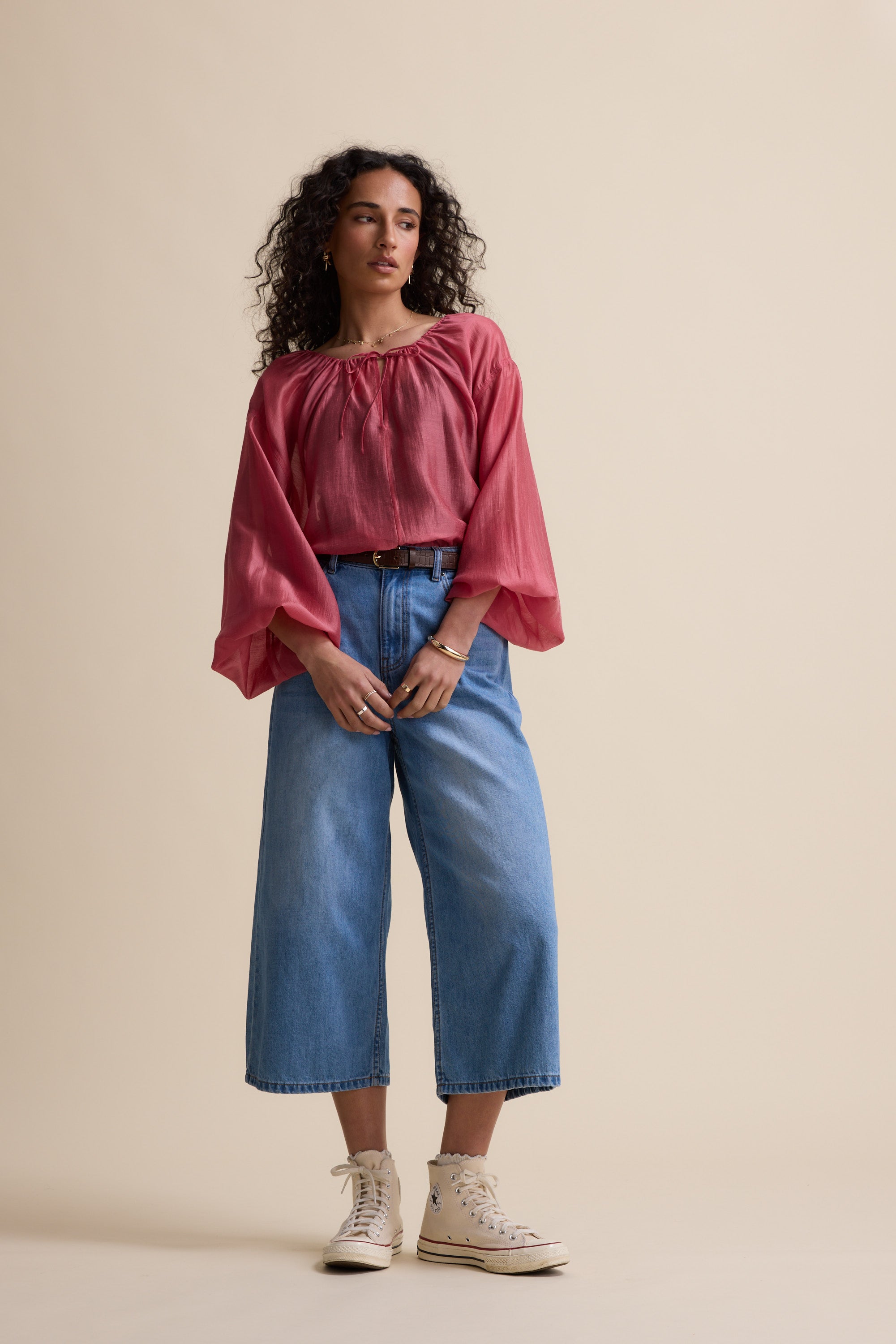 Woman in Max Abigail Tie Neck Blouse, wide-leg jeans, and sneakers against a beige background.
