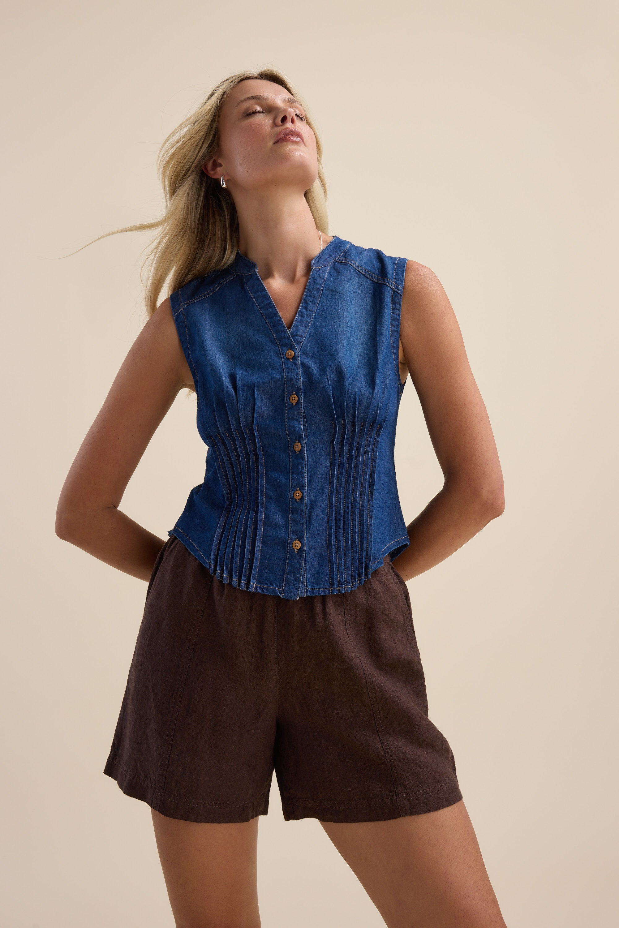 Woman in Max Brooklyn Tuck Detail Denim Shirt, brown shorts, neutral background.