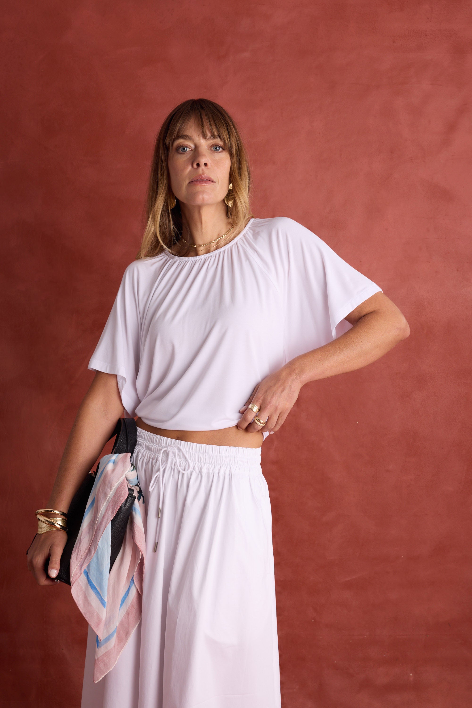 Woman in white poses, holding a Max Portia Silk Blend Square Scarf embellished bag.