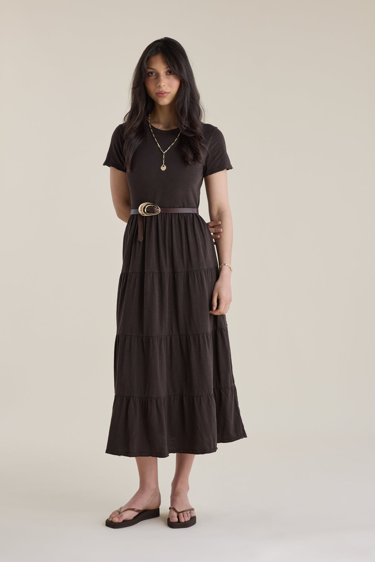 Woman in an Elementary Jersey Tiered Dress, necklaces, belt, and sandals, standing.